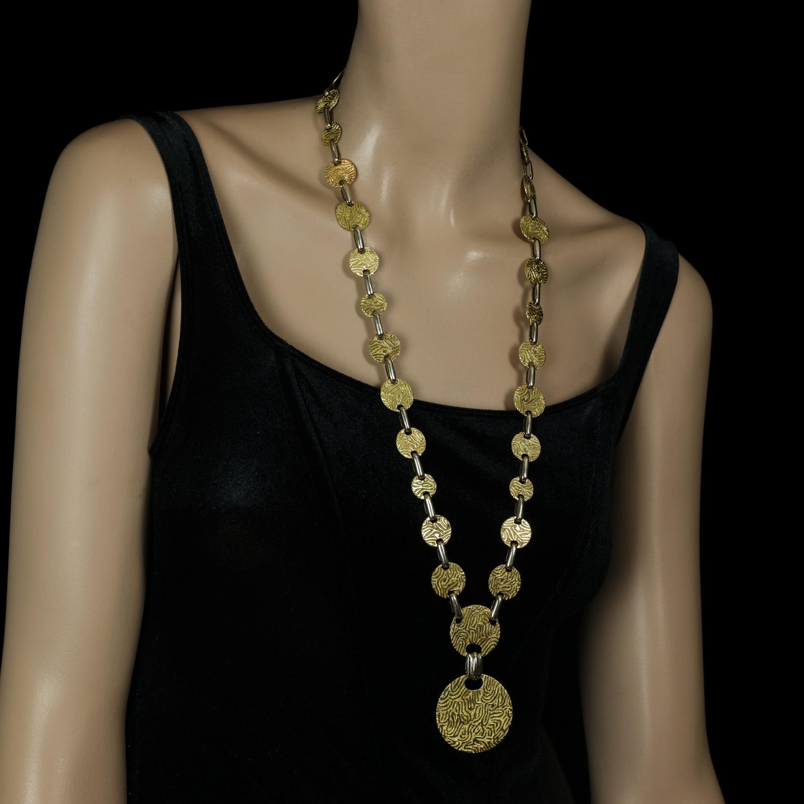 A bold long sautoir necklace by Cartier c.1960s composed of thirty circular discs of 18ct yellow gold with heavily textured abstract pattern on one side, the reverse plain polished, joined by uniform oblong white gold links, the centre hung with two