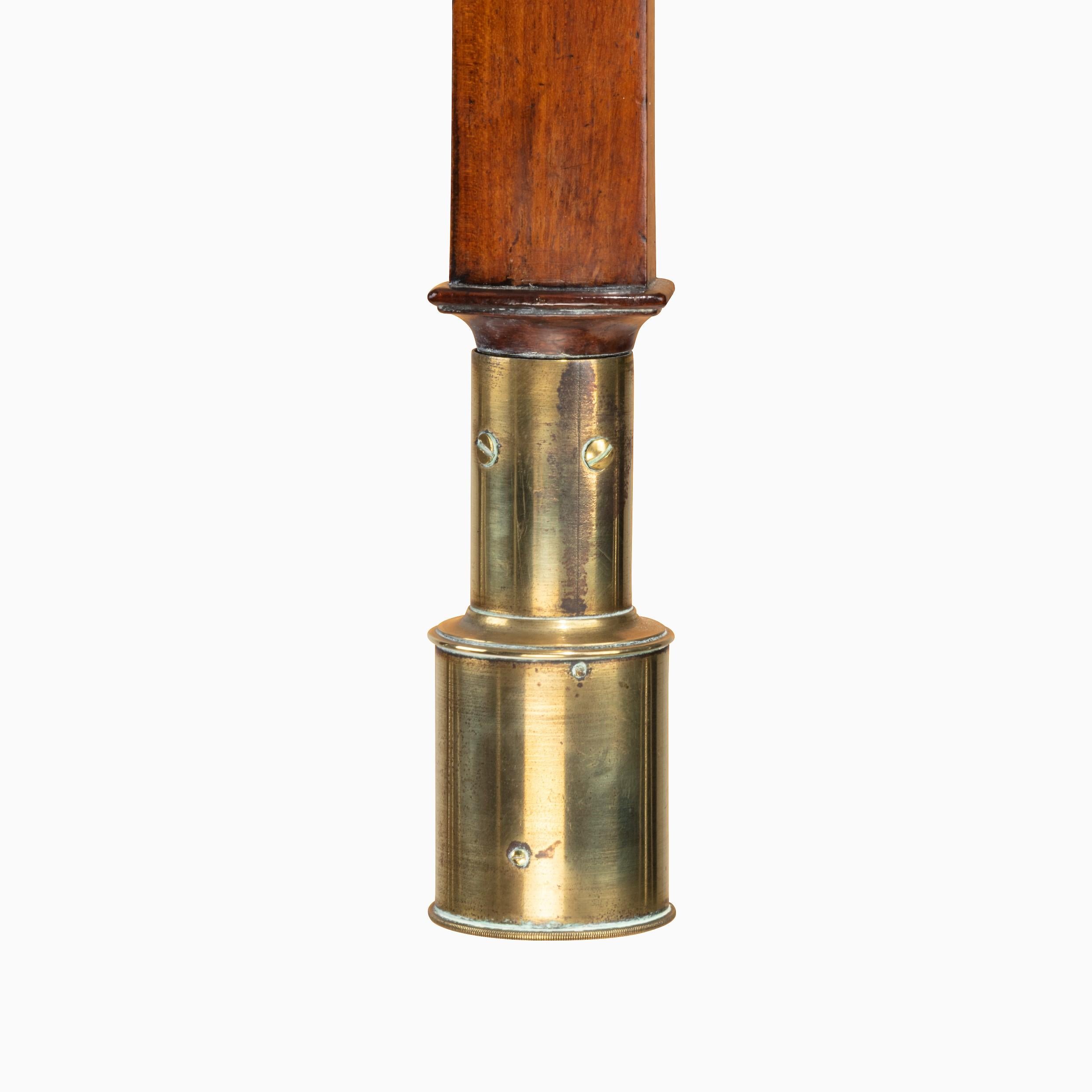 A bow-front marine barometer by John Dollond It is of slender cylindrical form with a silvered register plate enclosed by a hinged thermometer flap and mounted on a plain shaft. The brass gimbal weighted reservoir has pierced sides on the mounting.