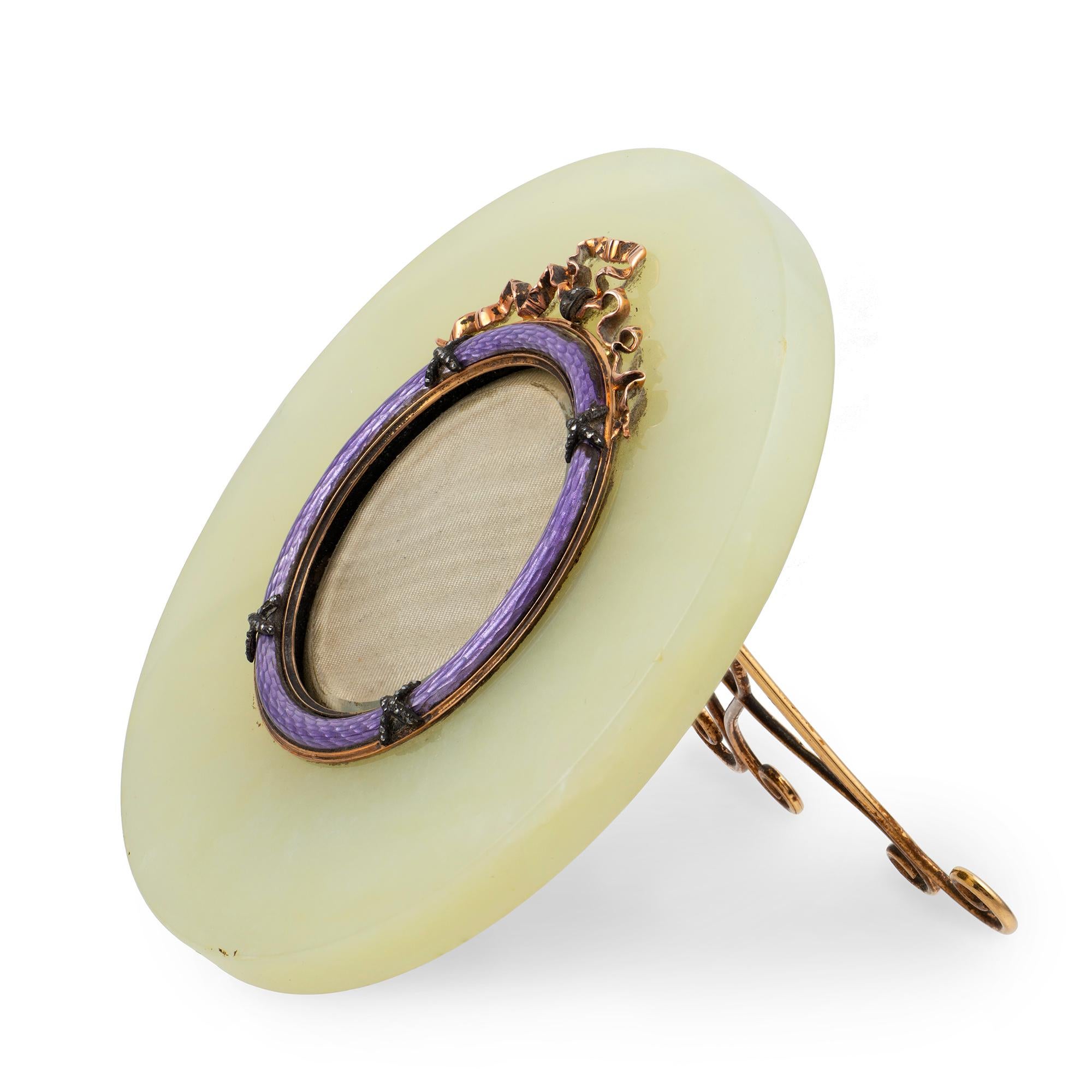 A jewelled gold-mounted bowenite and enamel frame, Fabergé, Michael Perchin, St. Petersburg, before 1899, the circular bowenite frame centred by translucent mauve bezel with applied diamond-set ties and ribbon motif, the reverse with gold scrolling