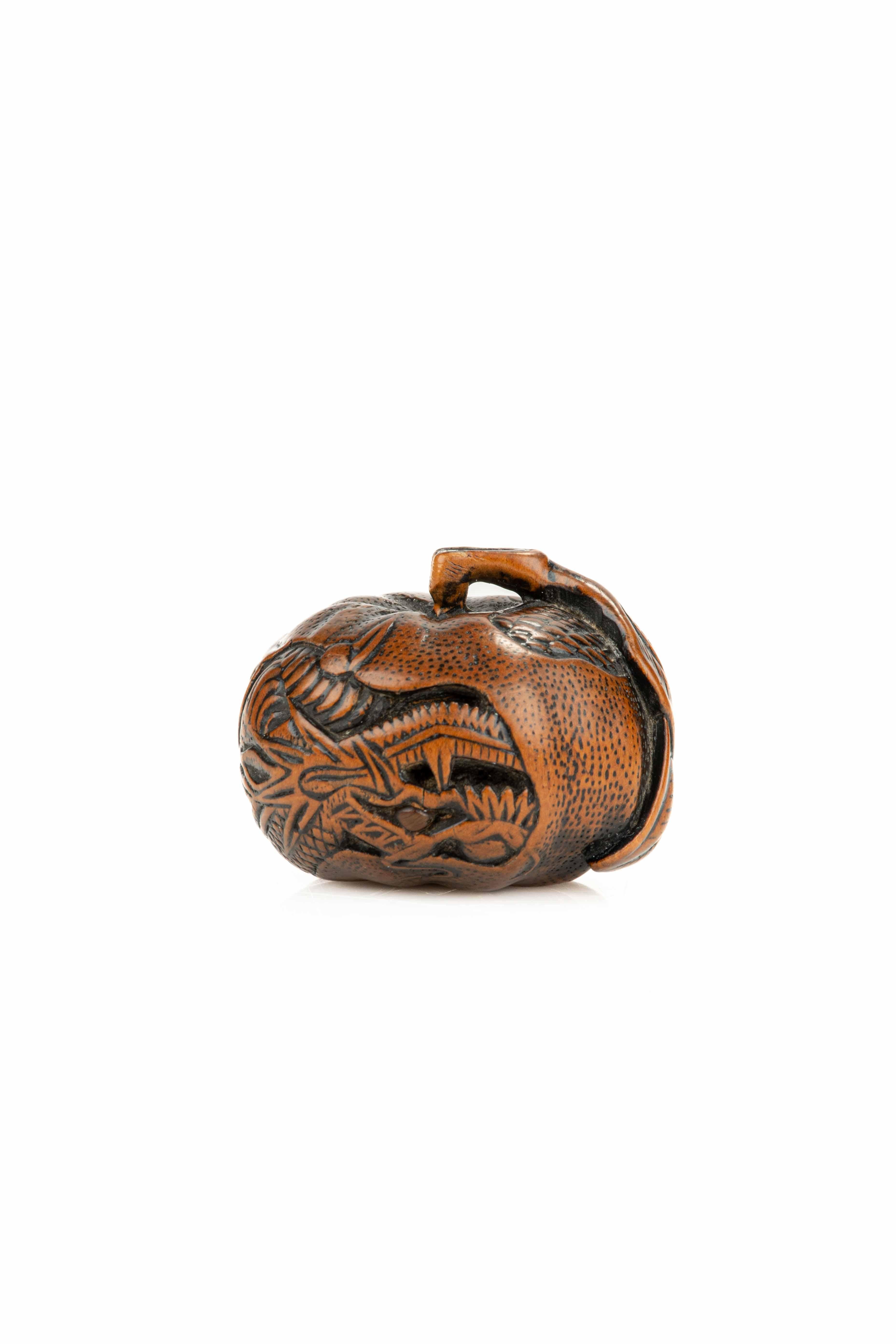 A boxwood netsuke depicting a mandarin fruit with a ryu dragon finely carved upside down, featuring a blonde horn-inlaid eye.  

Natural himotoshi formed from the mandarin’s stem, ending with two carved leaves on the side. 
Incised signature: