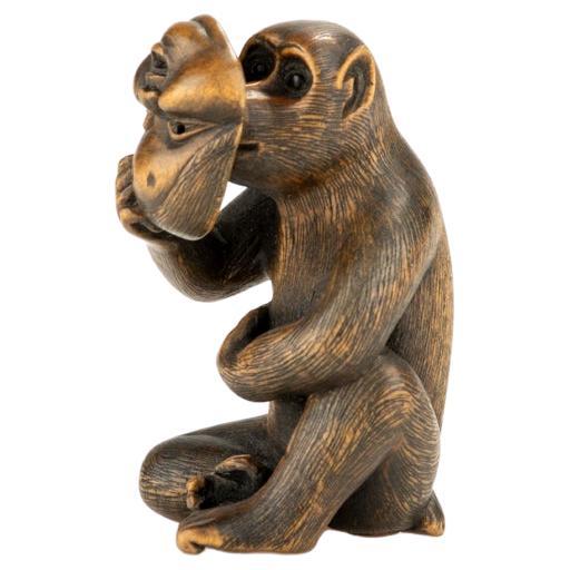 A boxwood netsuke depicting a monkey with an Okame mask, signed Shinzan For Sale