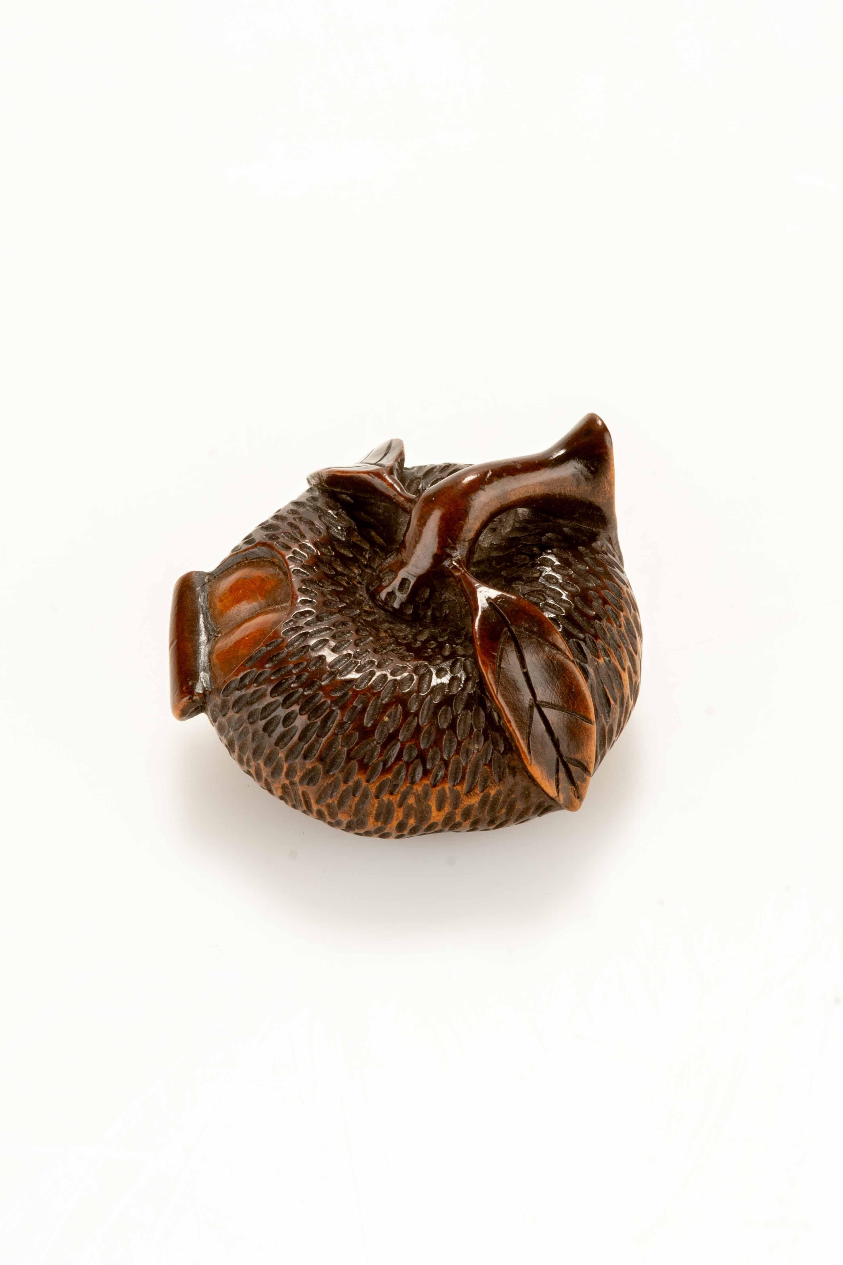 A boxwood netsuke depicting a partially peeled mandarin, carved with extraordinary realism. The peel reveals the segmented interior of the fruit, with every detail carefully defined. The texture of the peel and the veins of the leaves are