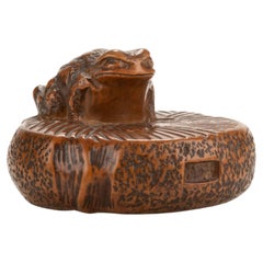 Netsuke de madera de boj que representa un sapo sobre una piedra de molino circular, firmado Masanao