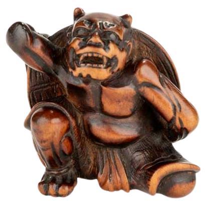 A boxwood netsuke depicting an Oni and the Setsubun festival