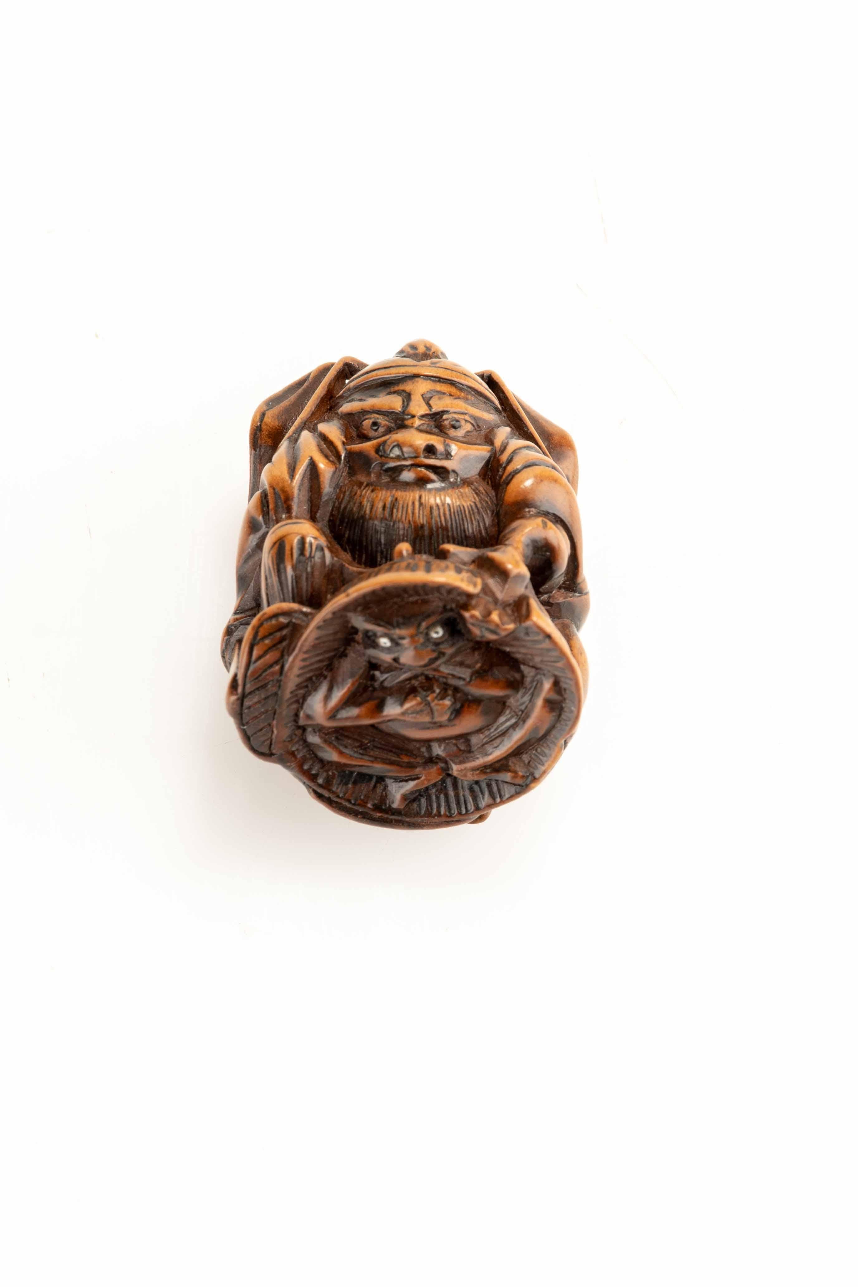 Un netsuke en buis représentant Shoki capturant un oni, le pressant sous un large chapeau de paille. 
Cette scène représente symboliquement la victoire du bien sur le mal. 

Période : Meiji, fin du 19e siècle 
Dimensions : 3 × 3,7 × 3,6 cm 
État :