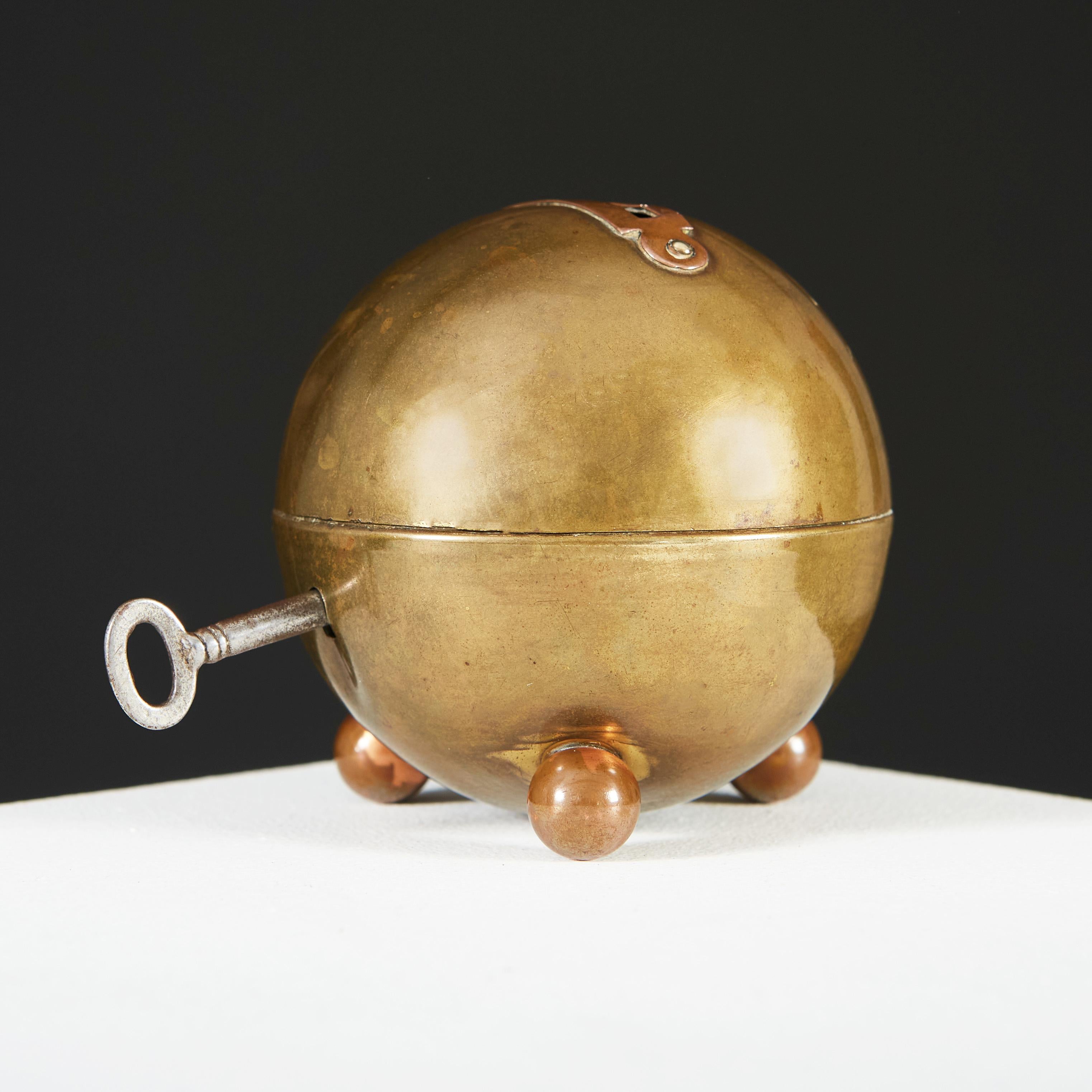 An early twentieth century brass and copper moneybox of spherical form, the brass body opening with lock and key, supported on three copper ball feet, with copper money slot to the top. Attributed to Marianne Brandt.

Marianne Brandt was a German