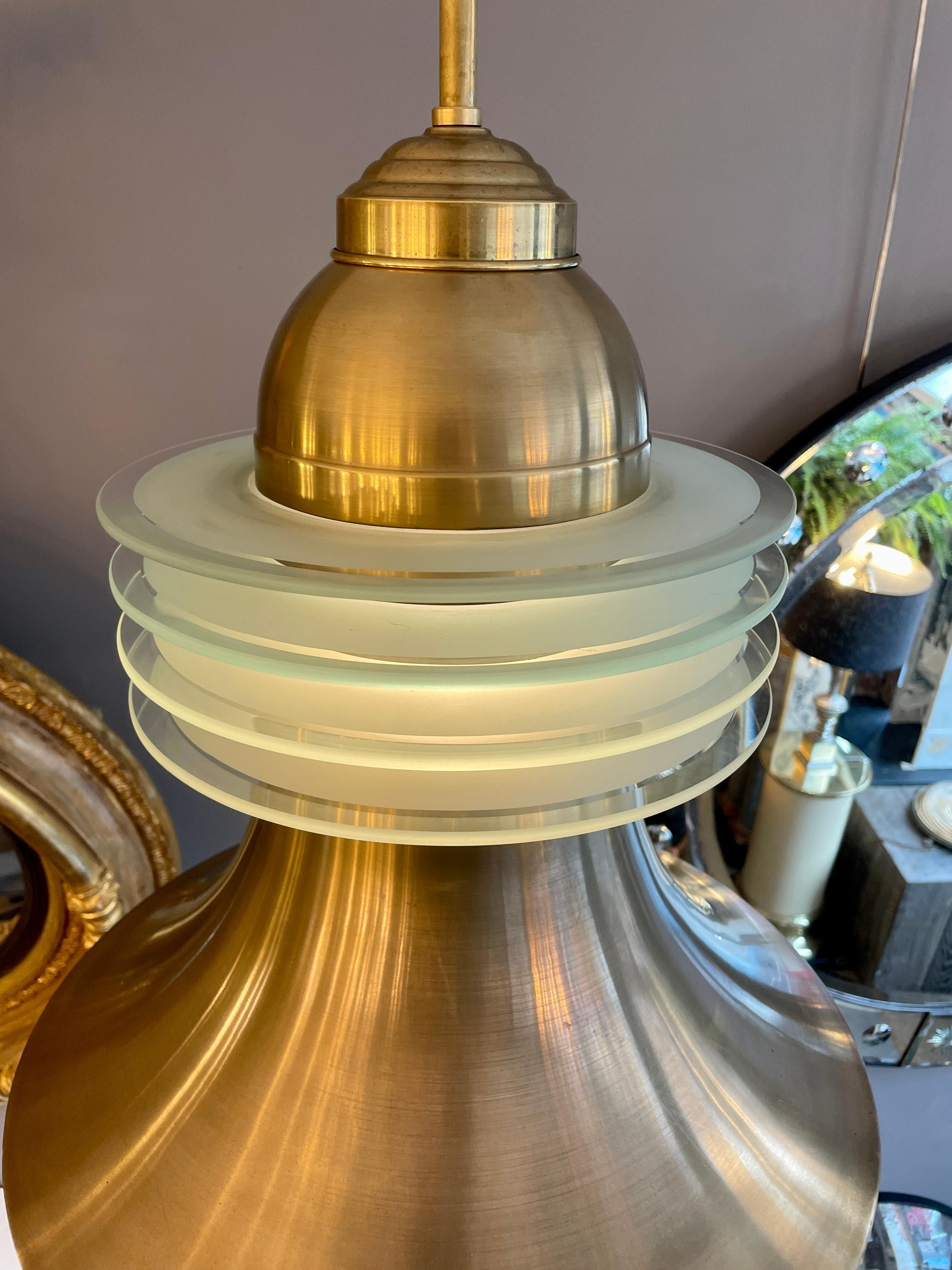 A brass and frosted glass pendant from the late Art deco to Mid Century period. The brass bell shaped light with four rings of frosted glass as a central diffuser, also lit from inside.