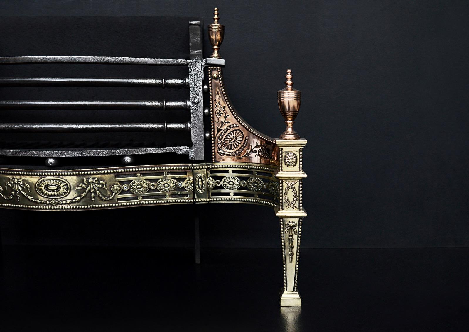 A decorative brass and gunmetal Georgian style fire grate. The pierced brass fret with paterae, swags and beading throughout, the tapering legs with laurel wreaths surmounted by turned finial. The gunmetal side-wings with beading and engraving.