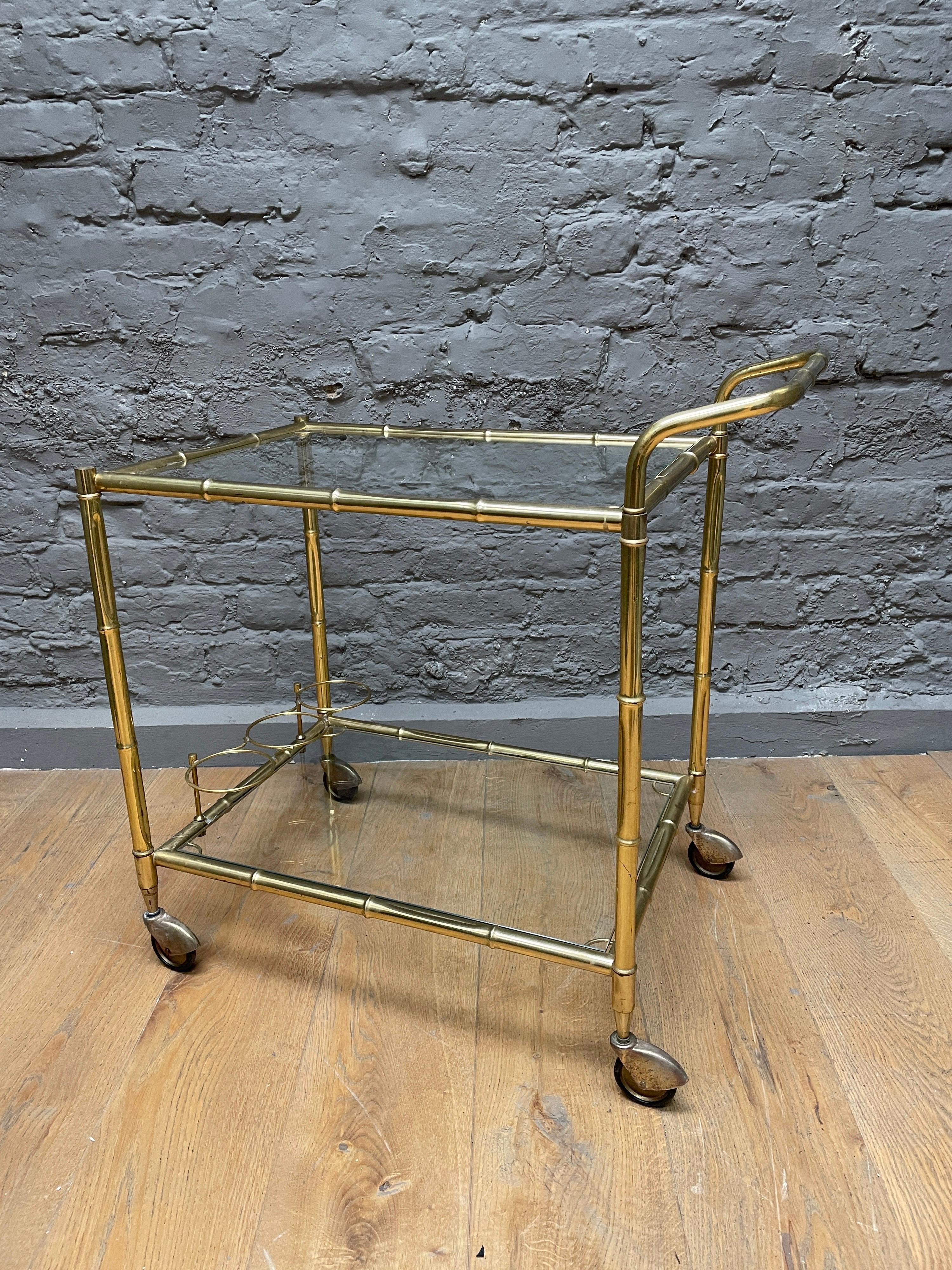 A two-tiered bar cart in brass faux bamboo with three-piece bottle holder on lower shelf.

French, circa 1960.