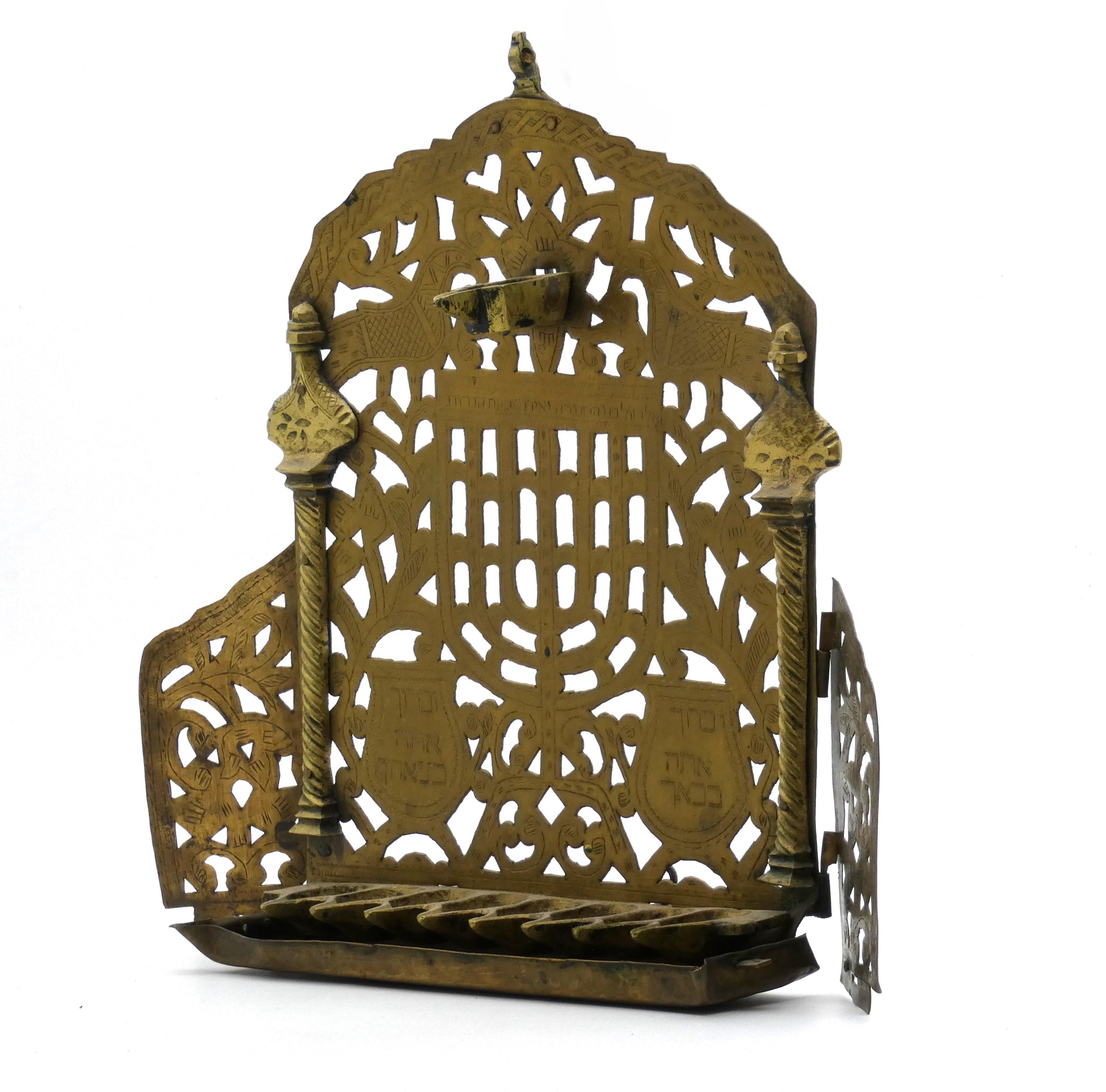 Moroccan brass Hanukkah lamp earnestly decorated with a menorah, columns, and verses.

Arched openwork foliate designed backplate, depicting a seven-branched menorah; a cornice inscribed with the verse 