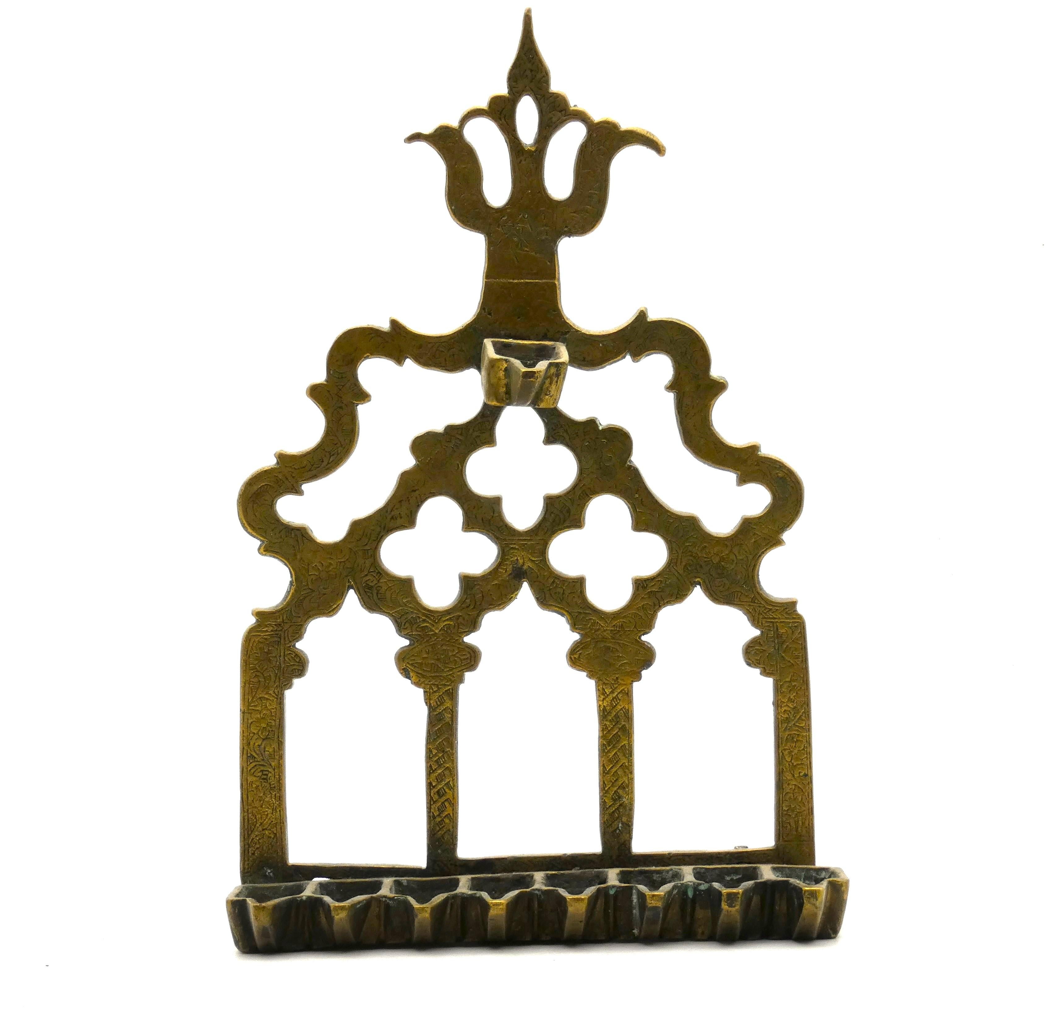 Hannukah lamp from Morocco made out of brass cast in the late 19th century.

The backplate for this menorah is built like the front of a structure with three doorways under three cloverleaf-formed windows, with two additional openings above them