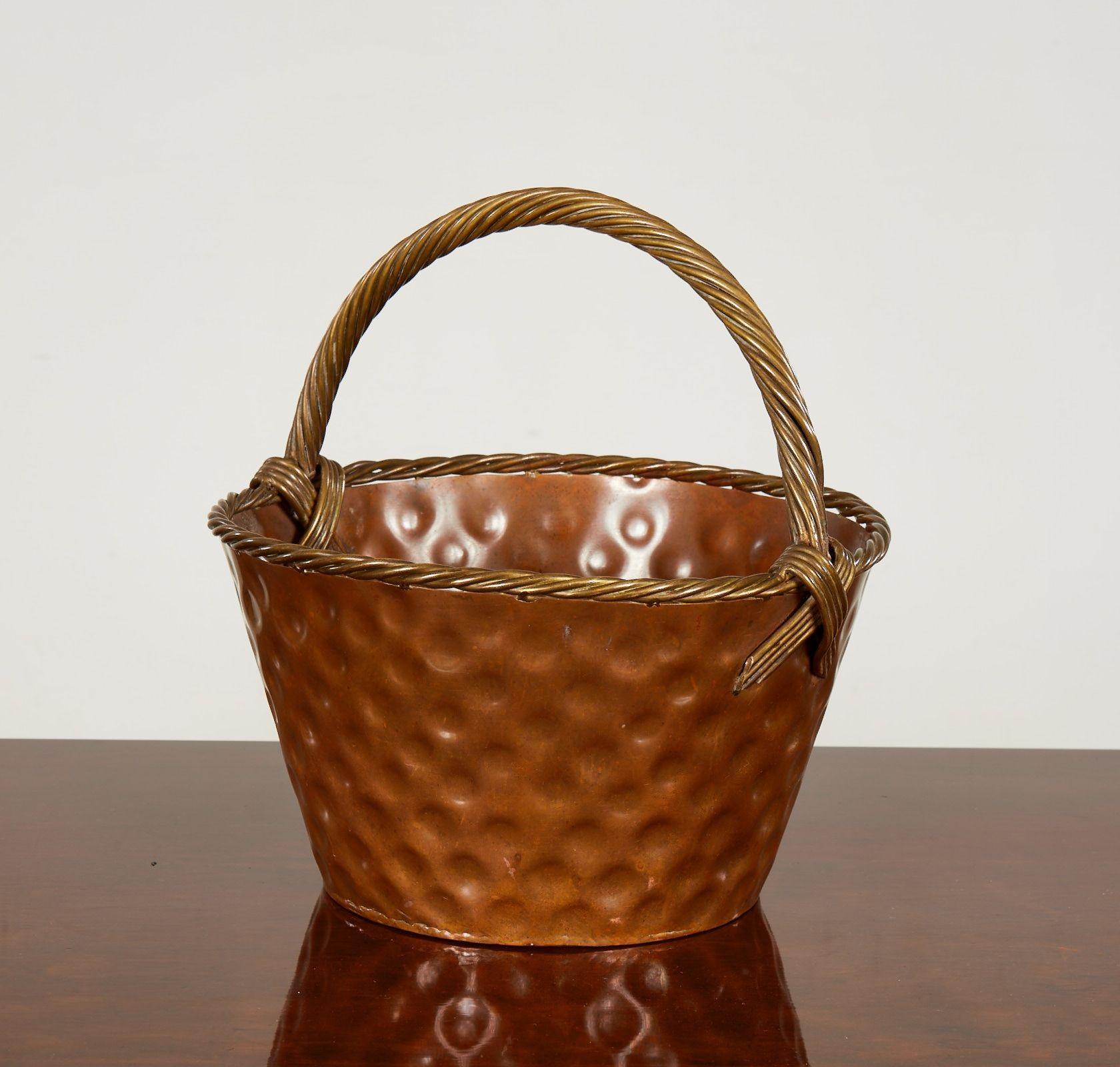 A brass basket with a marvelous faux rattan woven loop handle with cross-laid ends, a woven rim and a round, sloped body featuring large decorative dimples all around. Waterproof construction so can be used as a planter. English, circa 1930.
