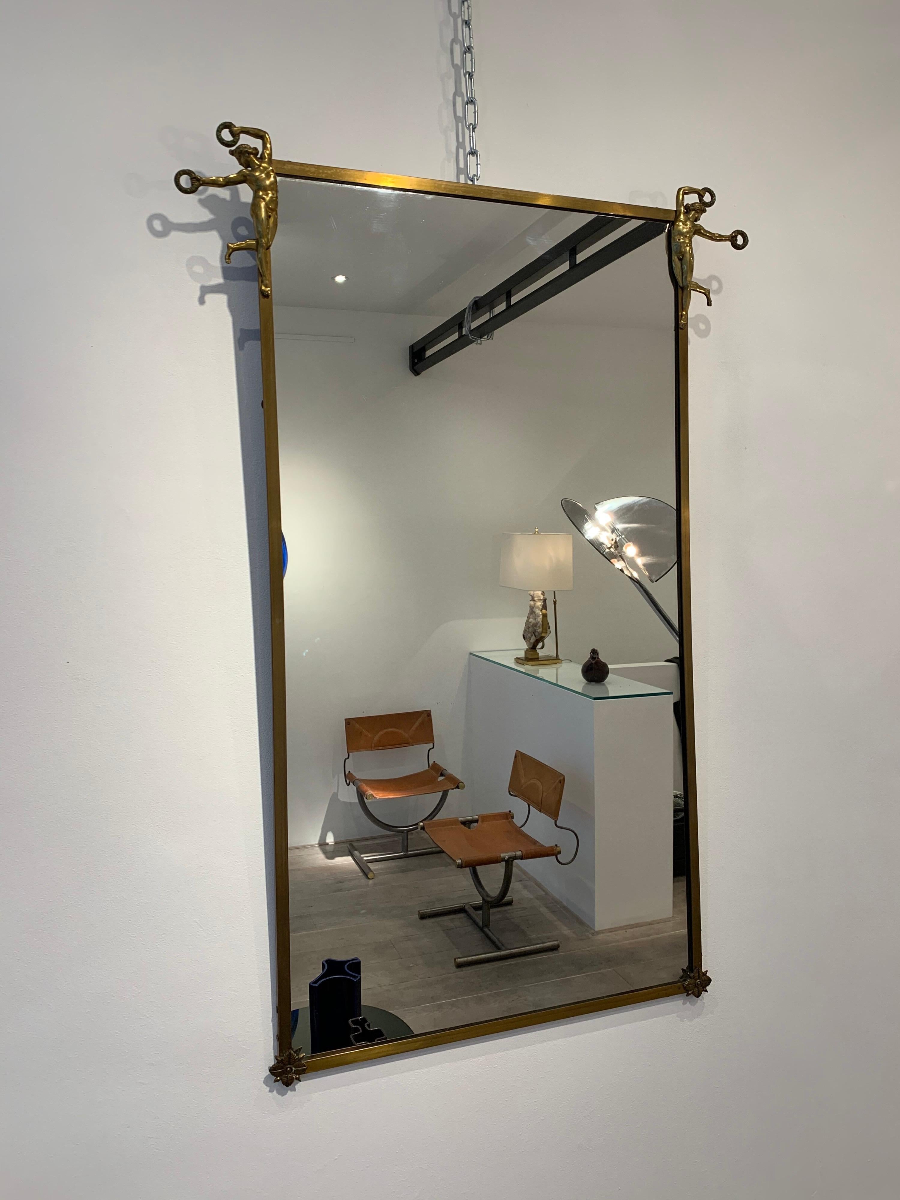 An elegant brass mirror with crowning at top Appollos and flowers decoration at bottom corners. The mirror is probably from French neoclassic inspiration, a style that was fully revived in the 1940s. The quality of the applied Appollos is beautiful.