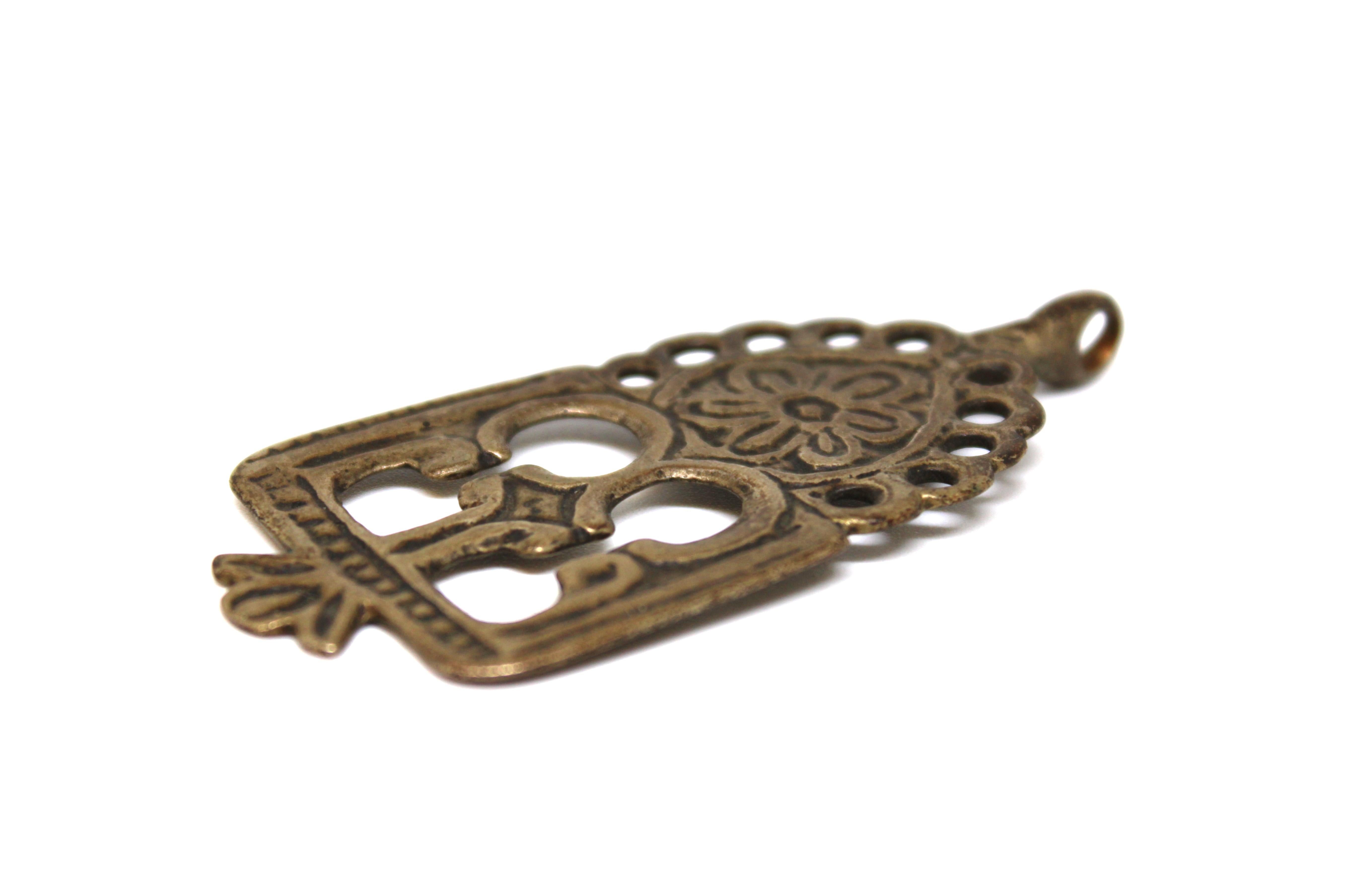 Cette amulette antique en laiton provenant du Maroc est une pièce unique et intrigante de l'art judaïque. Elle s'éloigne des formes conventionnelles de textes sacrés ou de symboles kabbalistiques que l'on trouve habituellement dans les amulettes. Au