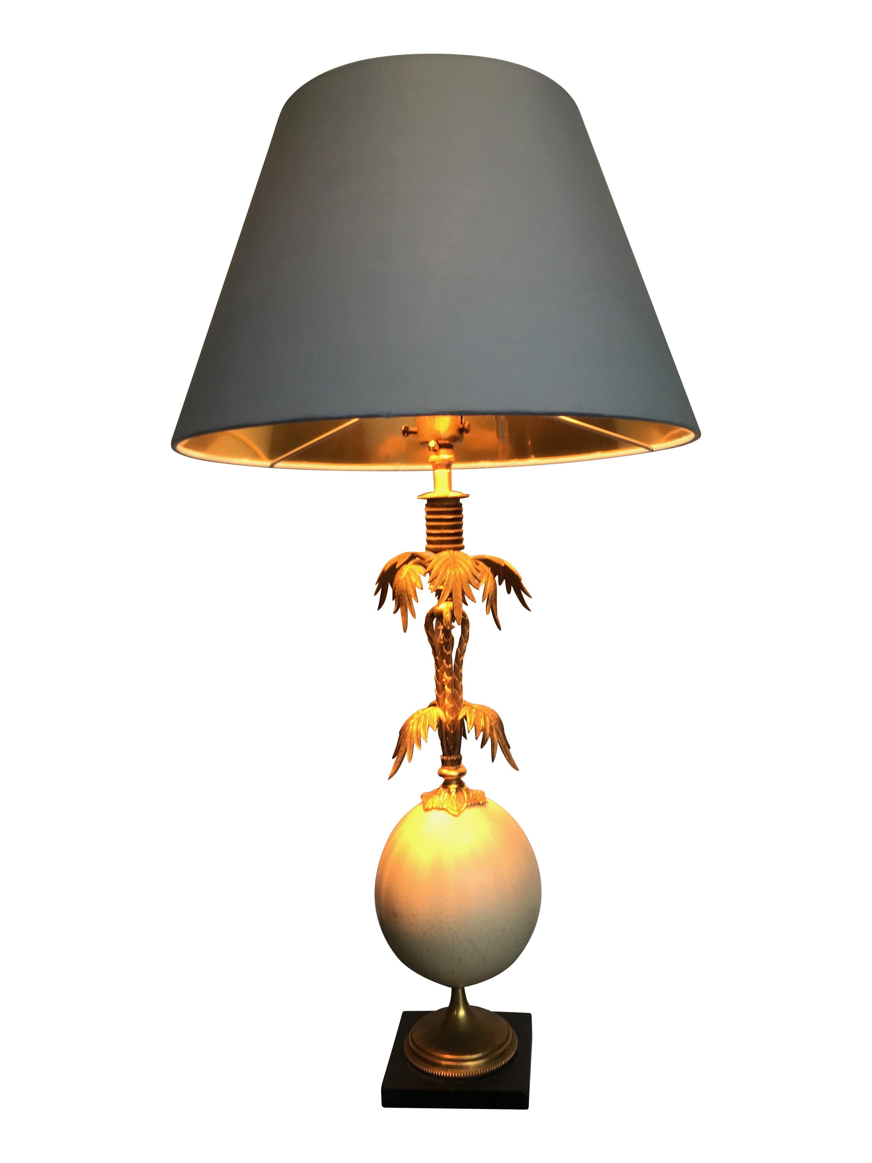 A brass palm tree table lamp with real ostrich egg centre mounted on a black slate base. With new bespoke ivory colored shade with gold lining.