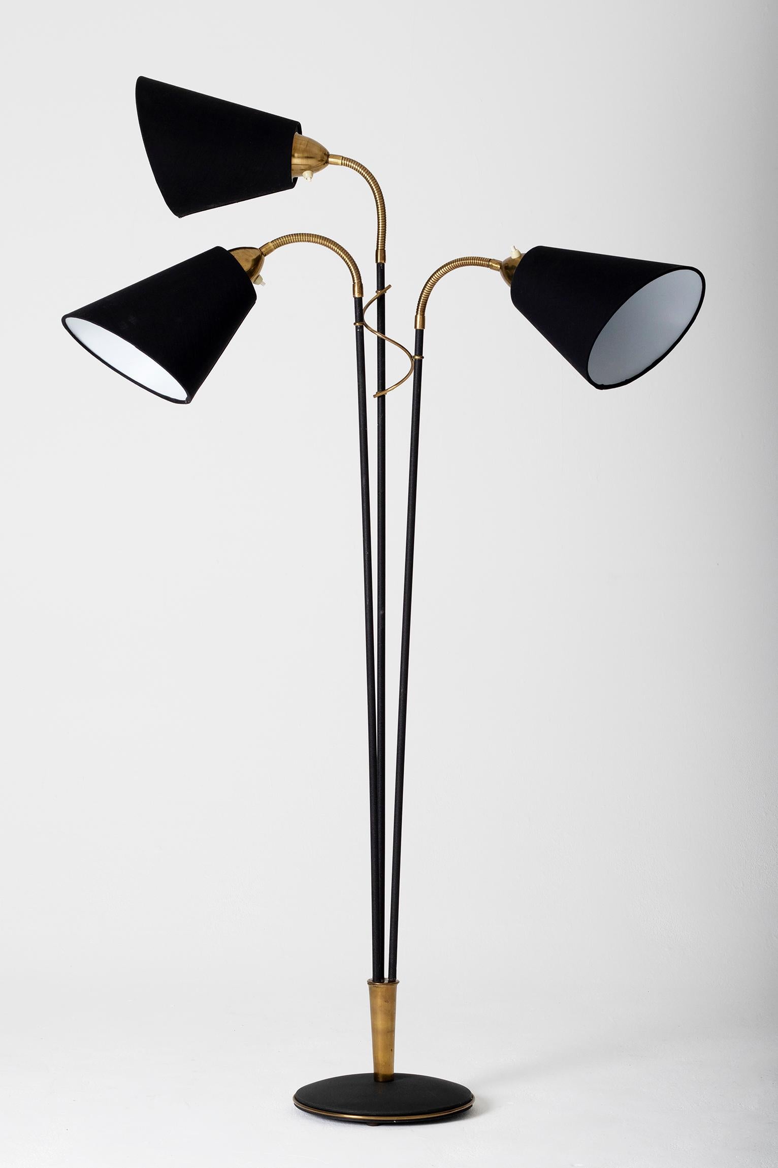 A brass and black enameled iron three-armed floor lamp, each light with its own switch, adjustable on brass gooseneck terminated with a black cotton angled shade.
Sweden, third quarter of the 20th century.
     
