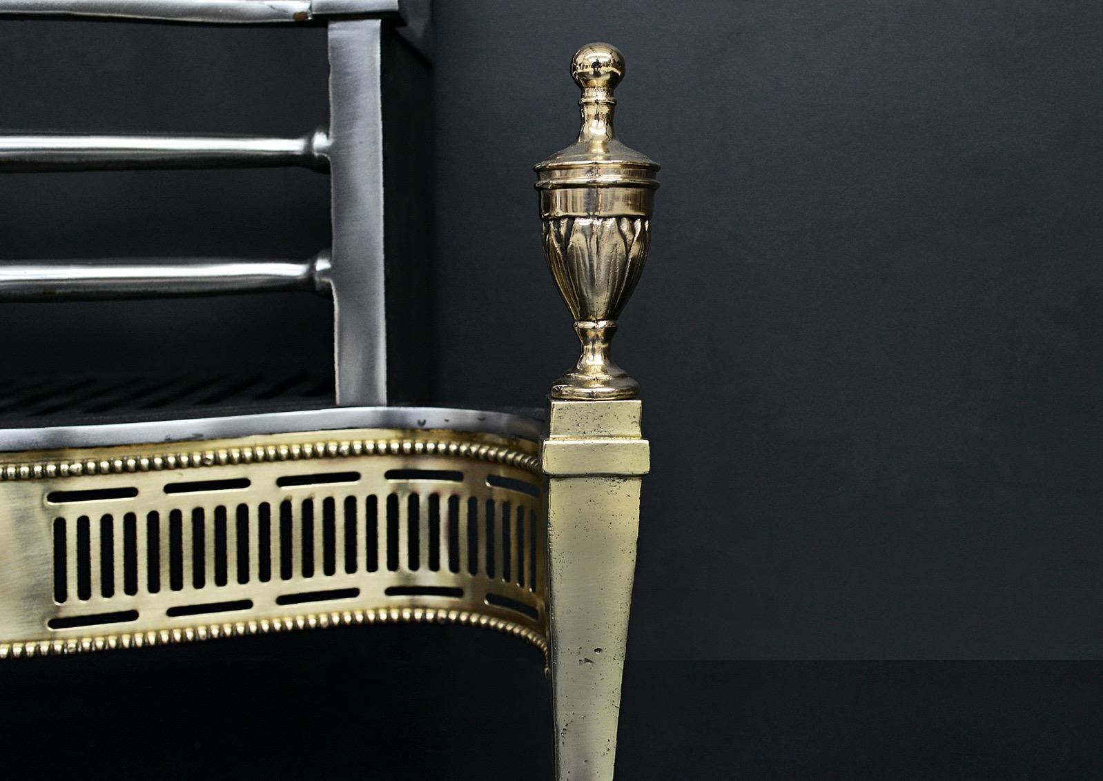 A brass and steel firegrate. The tapering legs surmounted by urn finials, the shaped fret with pierced fluting and beading. Bowed steel bars to burning area. Decorative cast iron fireback behind. English, 20th century. 

Width At Front:	615 mm     