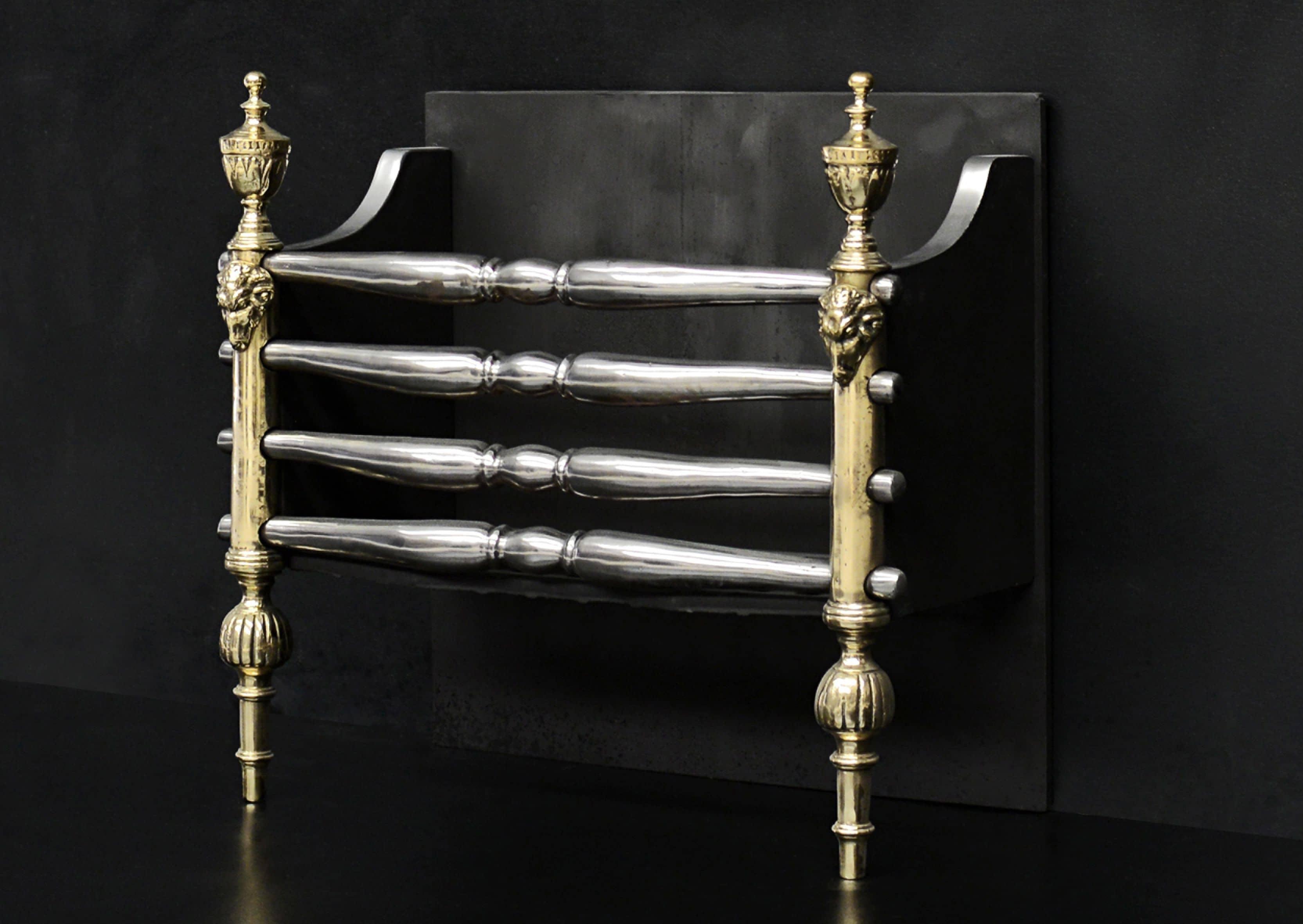 A brass and steel firegrate in the Regency style. The tapering feet surmounted by gadrooning, ram's heads and engraved brass finials. Shaped polished steel front bars with plain fireback behind. English, 19th century. 

Measures: Width at front: