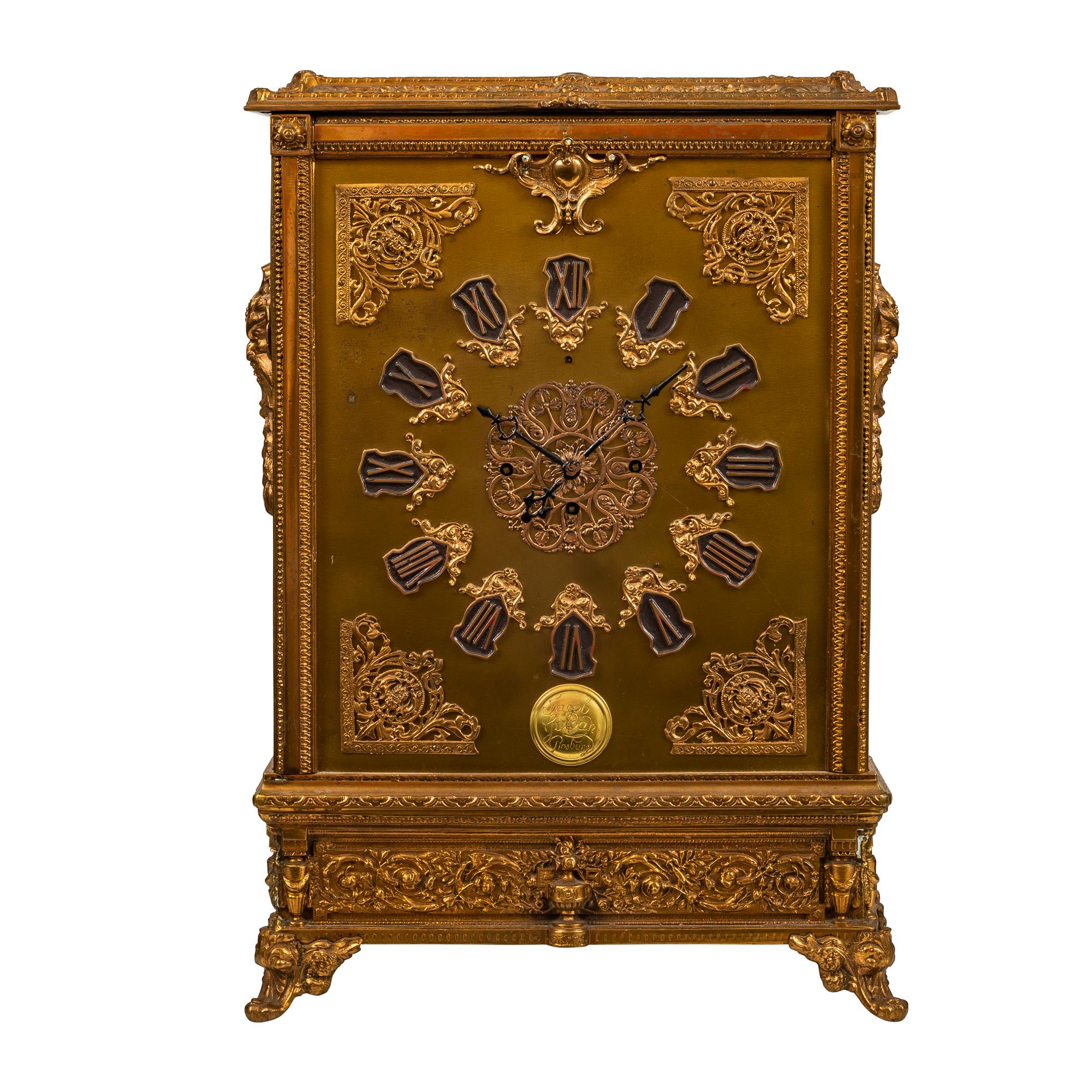 A brass table clock,Jacob Gulder, 20th century
9 1/2-inch dial with mask and scroll spandrels,the whole decorated in gilt with scrolls, trellis and masks
Measures: Height 20 in., width 14 in., depth 4 1/2 in. 
H 50.8 cm. , W 16.5 cm. , D 11.4 cm.