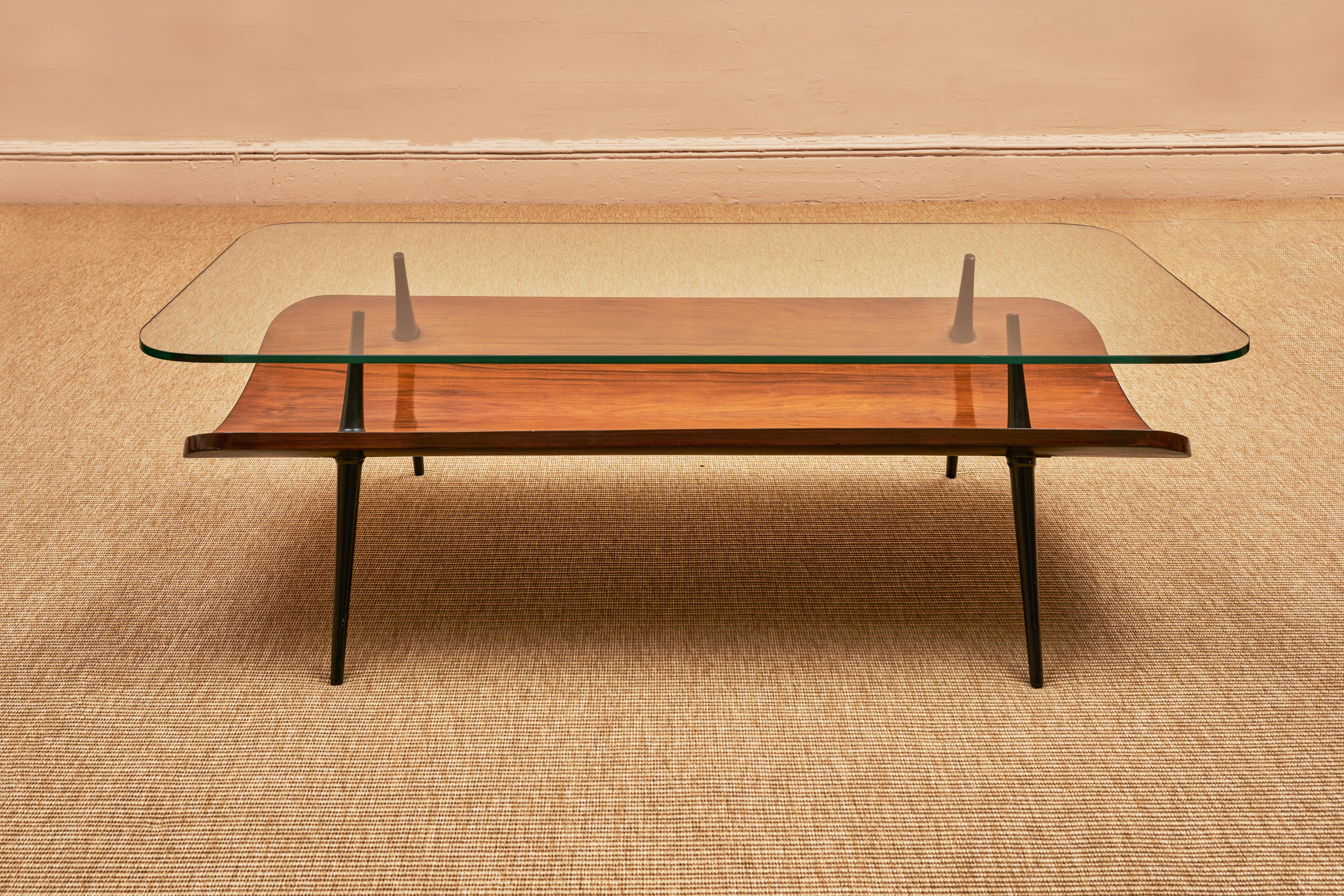 A Brazilan glass, walnut, and caviúna wood coffee table, circa 1950. This stunning piece features a rectangular glass top with a beautiful walnut and caviúna wood base. The reddish-brown hue of the caviúna wood complements the warm tones of the