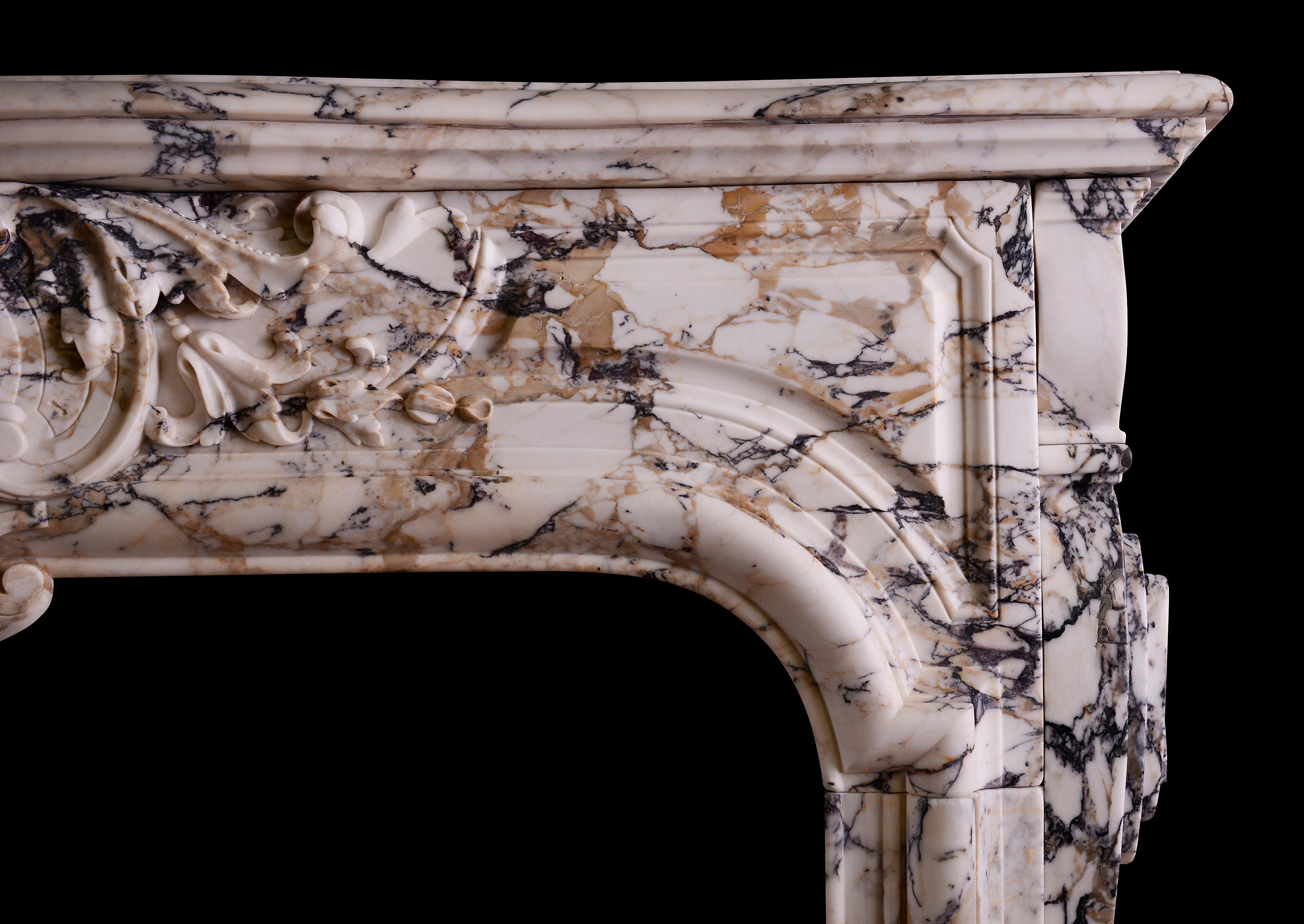 A Fine quality period French Louis XIV/XV transitional fireplace in Breche Violette marble. The moulded jambs with carved brackets to outgrounds. The arched, panelled frieze with cartouche to centre, flanked by foliage and scrollwork. Moulded shelf