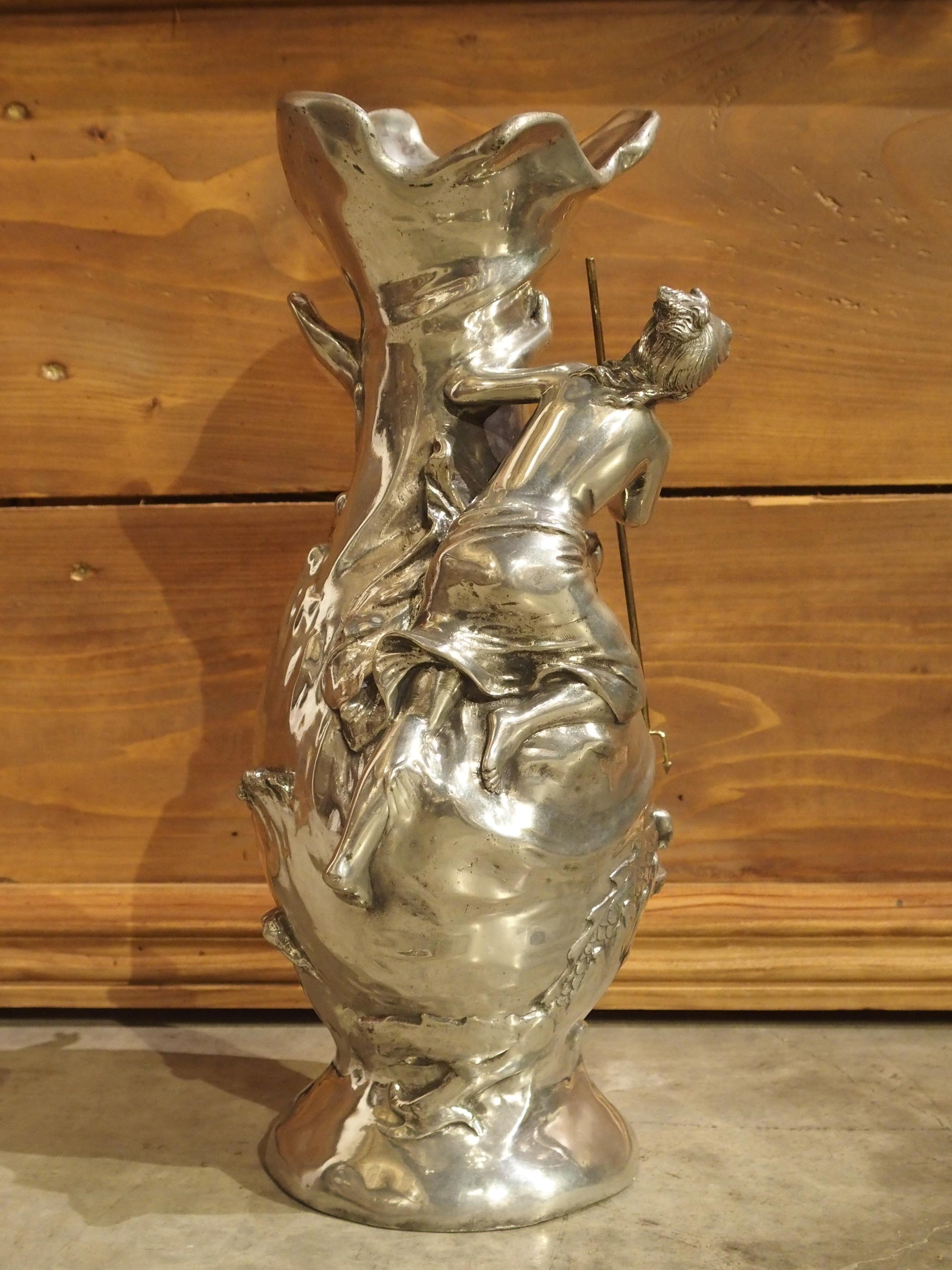This French vase is made from a bright pewter and depicts a woman fending off a sea monster. A putti is opposite her peering down at the swimming creature. There is fantastic movement which is shown as raised and swirling shapes of water. It is from