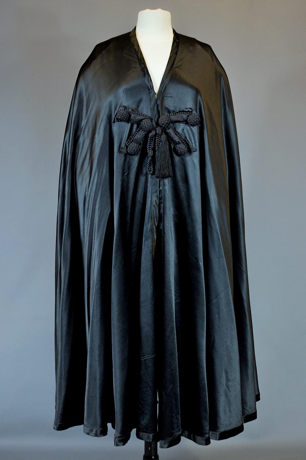 Circa 1920/1940

England

Beautiful evening cape or oriental Burnous in Duchesse silk satin black labelled Bradley 1870, Court Dressmaker, Chepstow Place, Bayswater, London W. Large cape and false hood adorned with a black silk trimmings pompom with