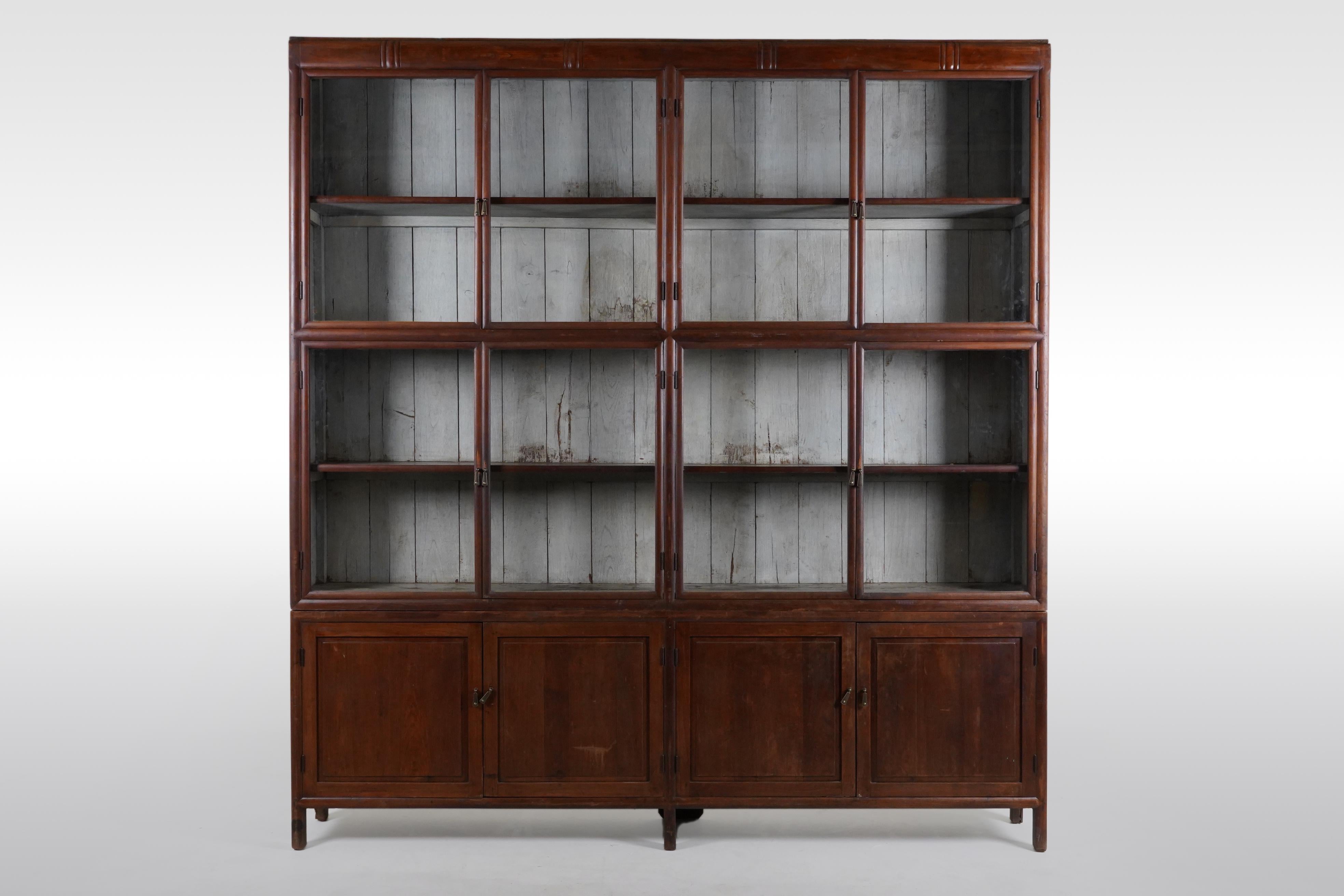 This impressively book cabinet was made from solid Teak wood and dates to the 1940's. The cabinet is made in two sections; an upper part with  glass doors and four levels for display of books and artifacts and a lower part with solid hardwood doors