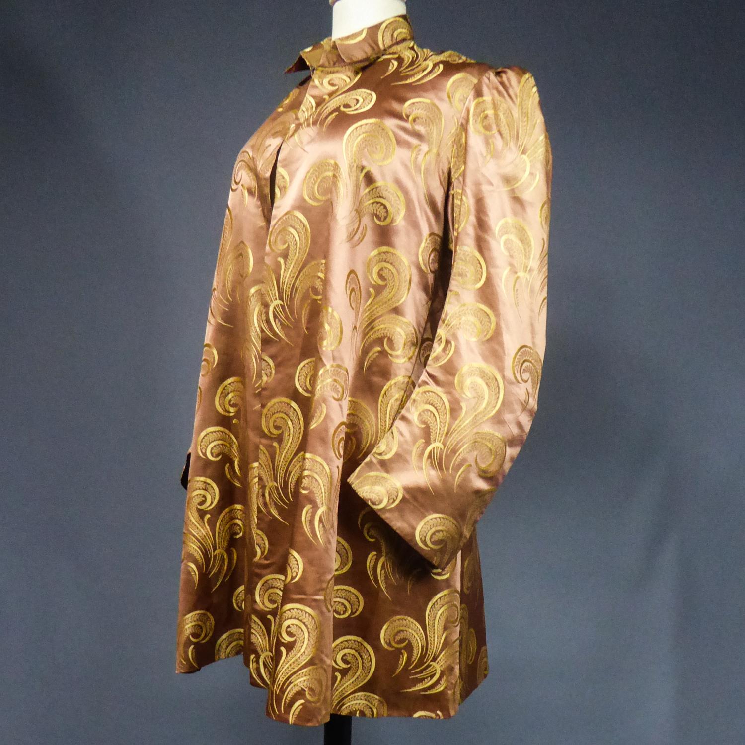 Circa 1930/1950
France

Superbe veste de soirée ou de fête inspirée du style Amazone, en satin de soie marron avec des motifs stylisés dorés en volutes, plumes et panaches. Il s'agit d'une réutilisation d'une robe plus ancienne car le satin de soie