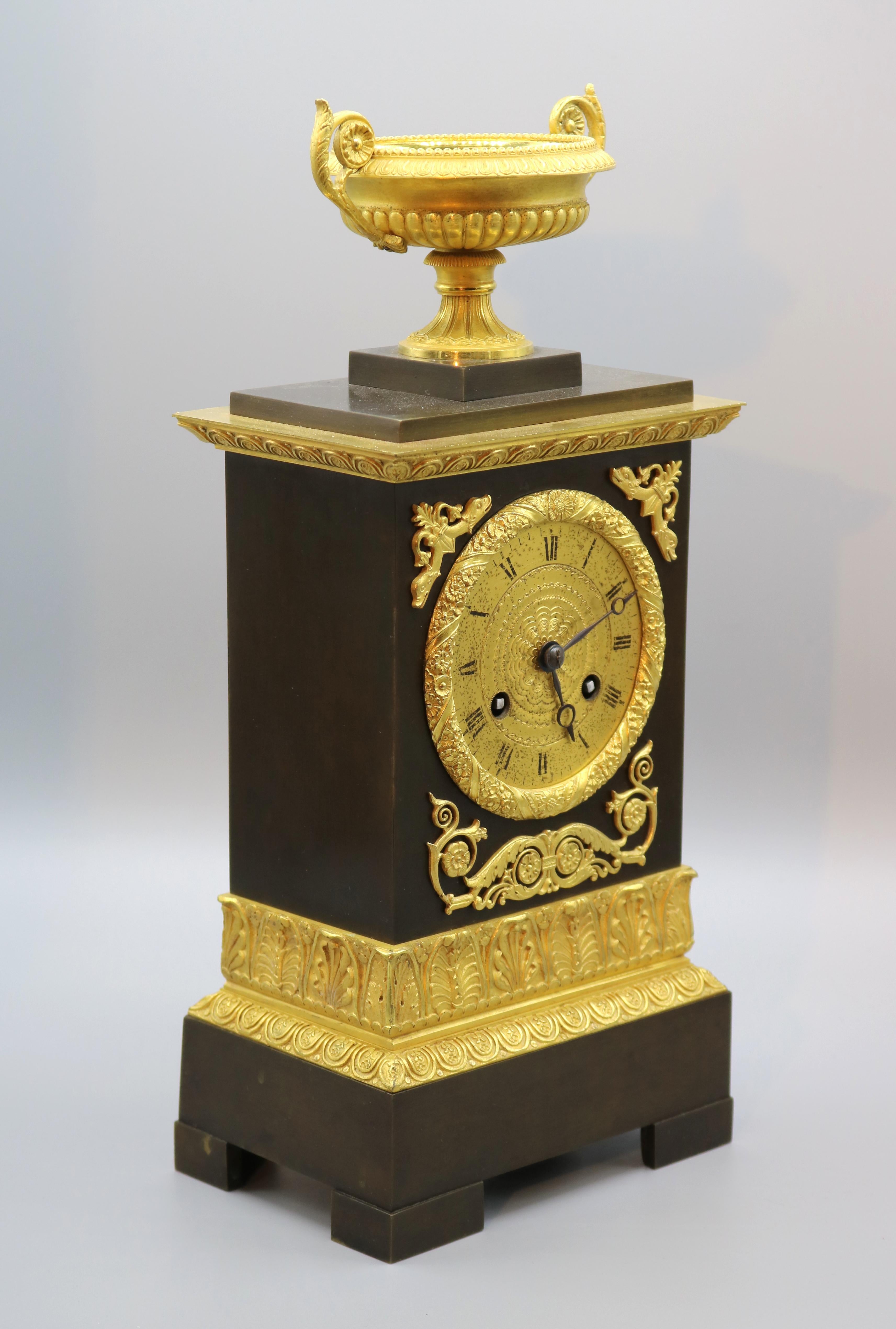 An early 19th century French bronze and ormolu eight day silk suspension striking clock contained in ornate case surmounted by well-cast and gadrooned urn with scroll carrying handles.