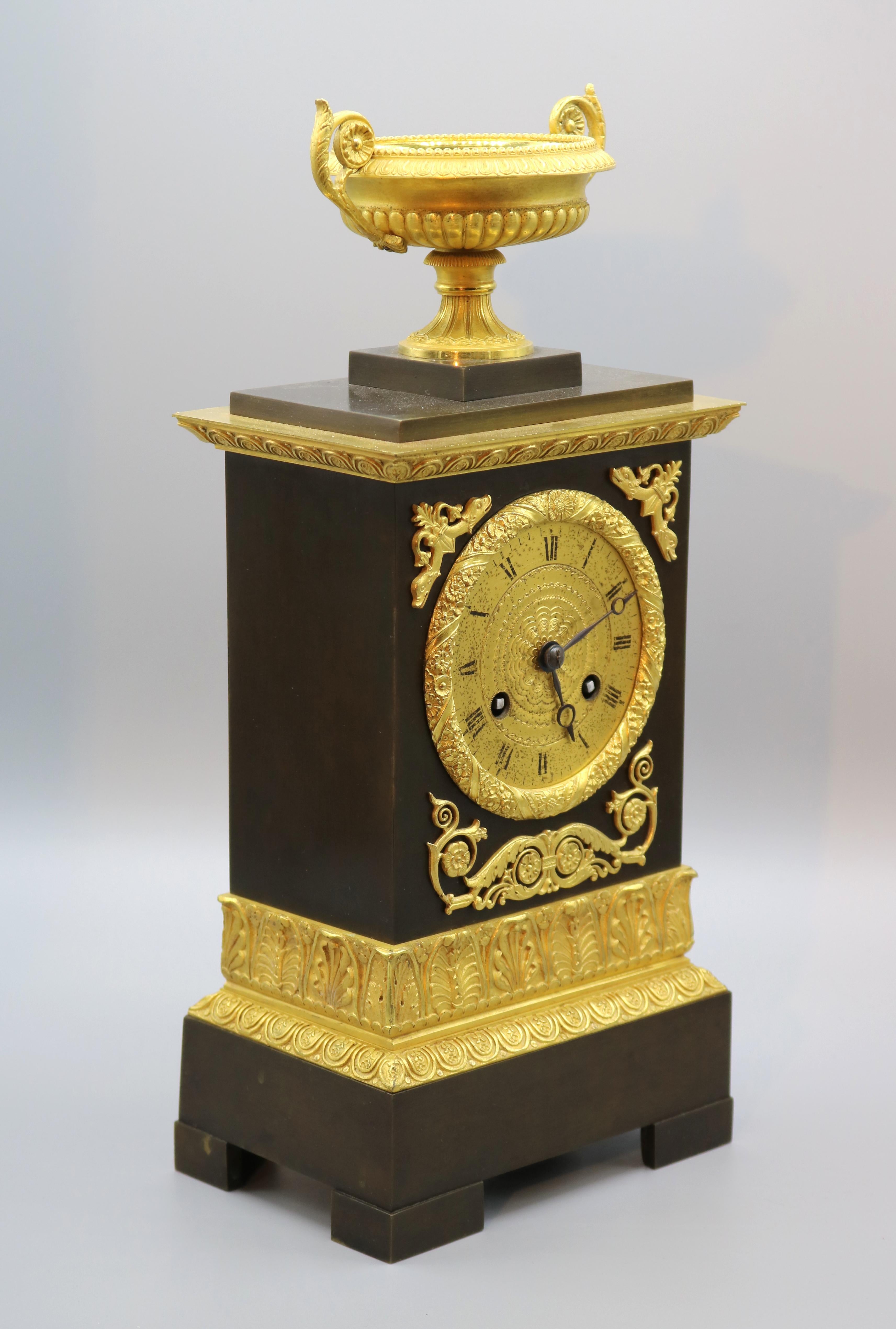 Orologio francese di inizio Ottocento in bronzo e ormolu con suoneria a sospensione in seta di otto giorni, contenuto in una cassa ornata e sormontata da un'urna ben fusa e lavorata con manici a voluta.
