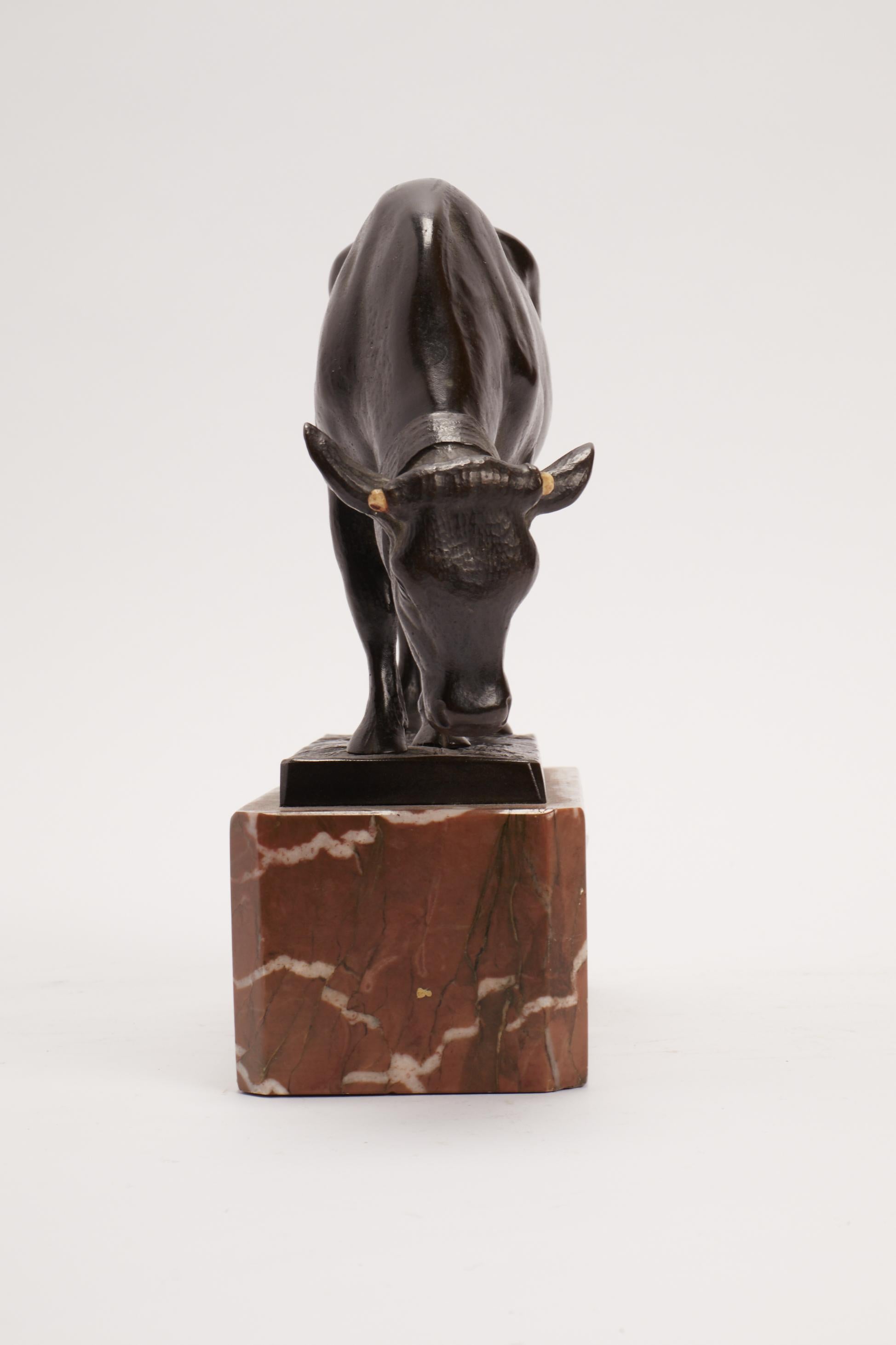A lost wax bronze sculpture depicting a cow grazing on a meadow, on a Verona red marble base. The cow's horns are made of bovine horn. Signed Moseritz. France circa 1880.