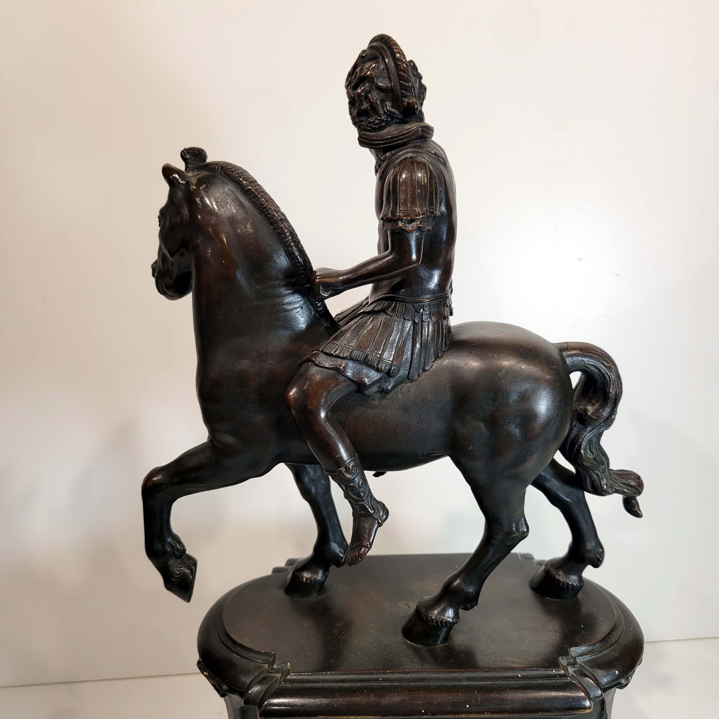 The rider in Roman armour and with his head turned to dexter; the horse pacing. After Riccio, Circa 18/19C. Lost wax casting in greenish black patina and reddish highlights. The base is cast bronze with two different relief panels on each side and