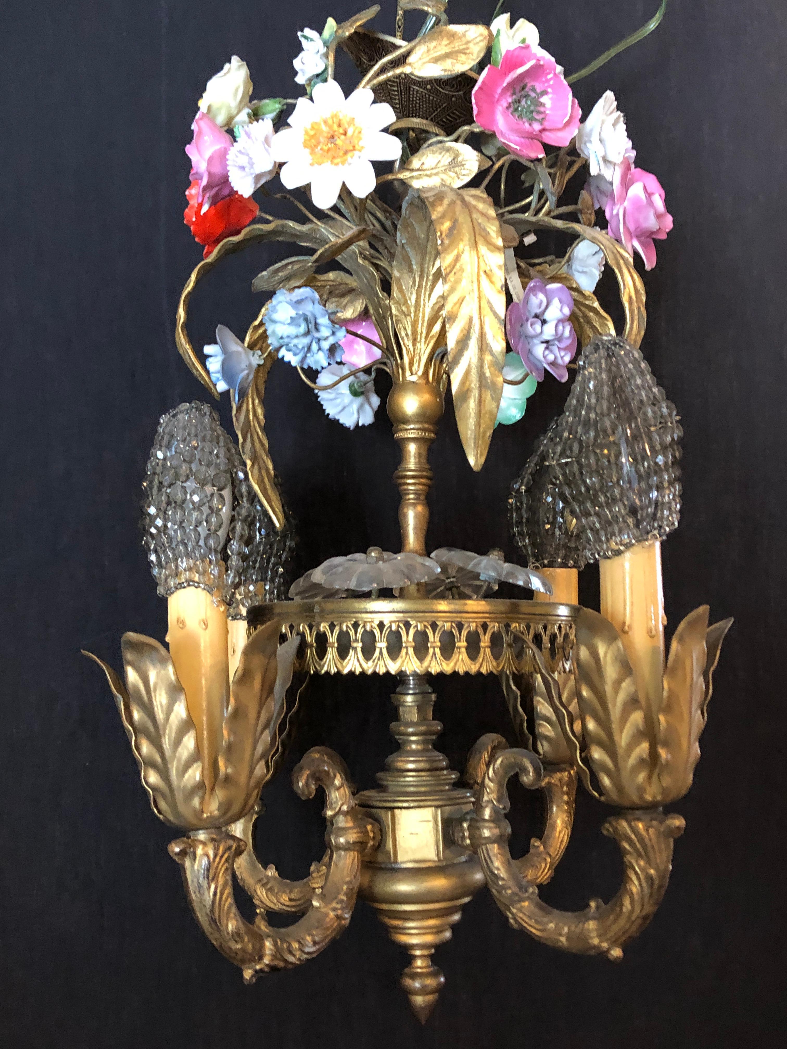 A bronze Louis XVI style French chandelier with porcelain flowers. This nicely cast small chandelier has four lighted arms with beaded shades that go over the bulbs. The center post having several Lalique style flowers which have a stem posting from