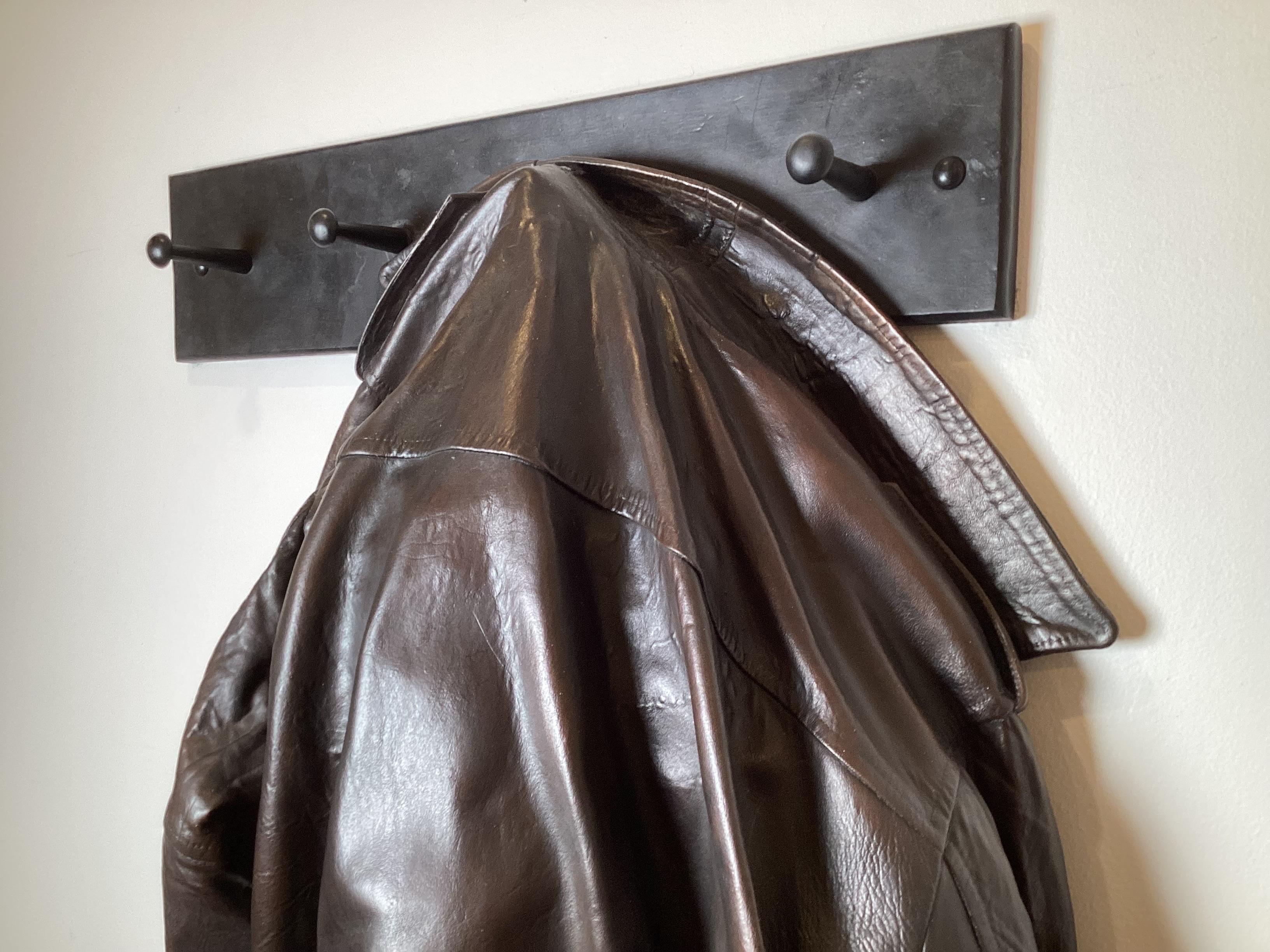 A unique patinated bronze sculpture in the form of a 1940's leather bomber jacket hanging on a wall mounted coat rack. The 1940's bomber jacket. It is one of the few items that has really transcended both fashion and trends. People are wearing these