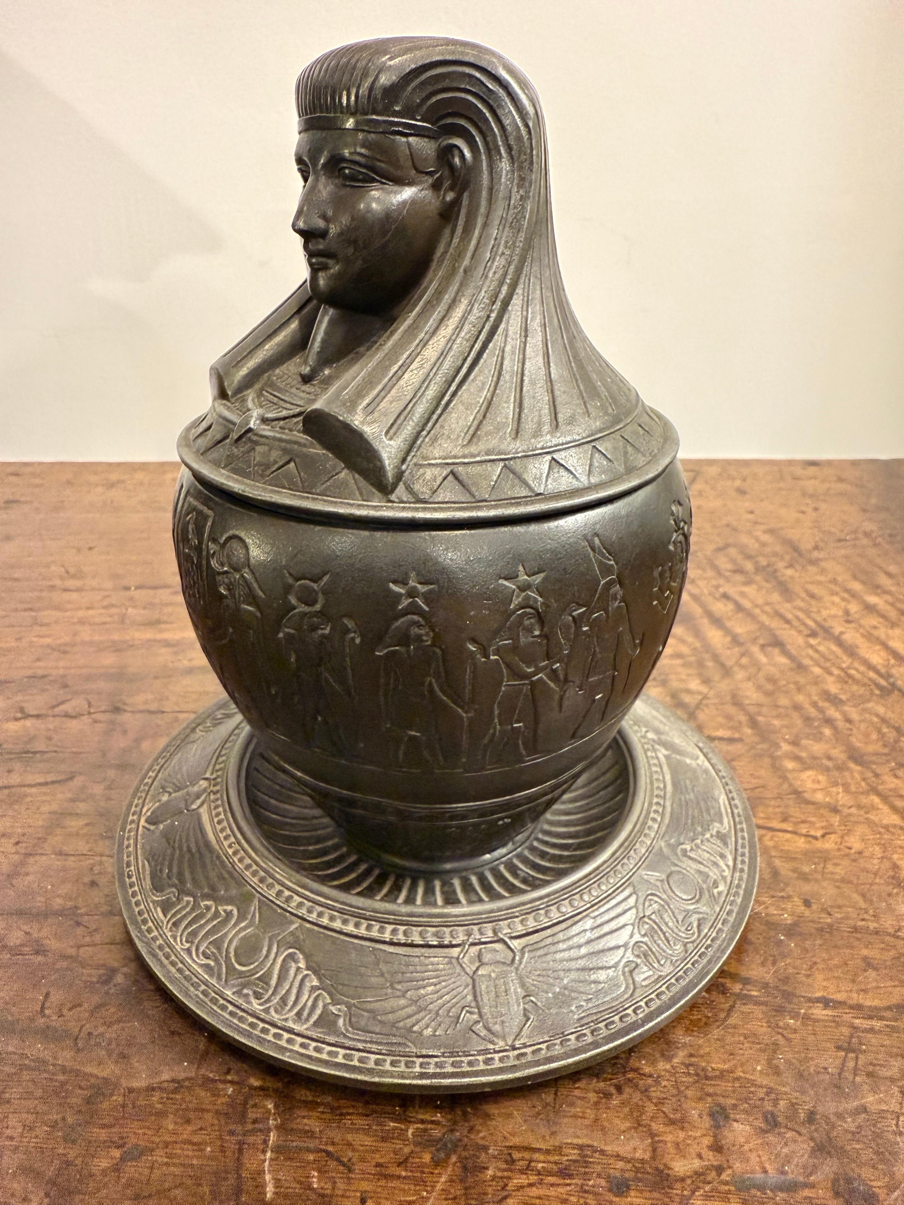 Vaso canopo in metallo bronzato, inizio XX secolo

Provenienza: Collezione privata australiana Acquistata a Roma nel 2007.

Descrizione:
Il vaso di bronzo con coperchio ha la forma di una testa umanoide che indossa il copricapo faraonico nemes e la