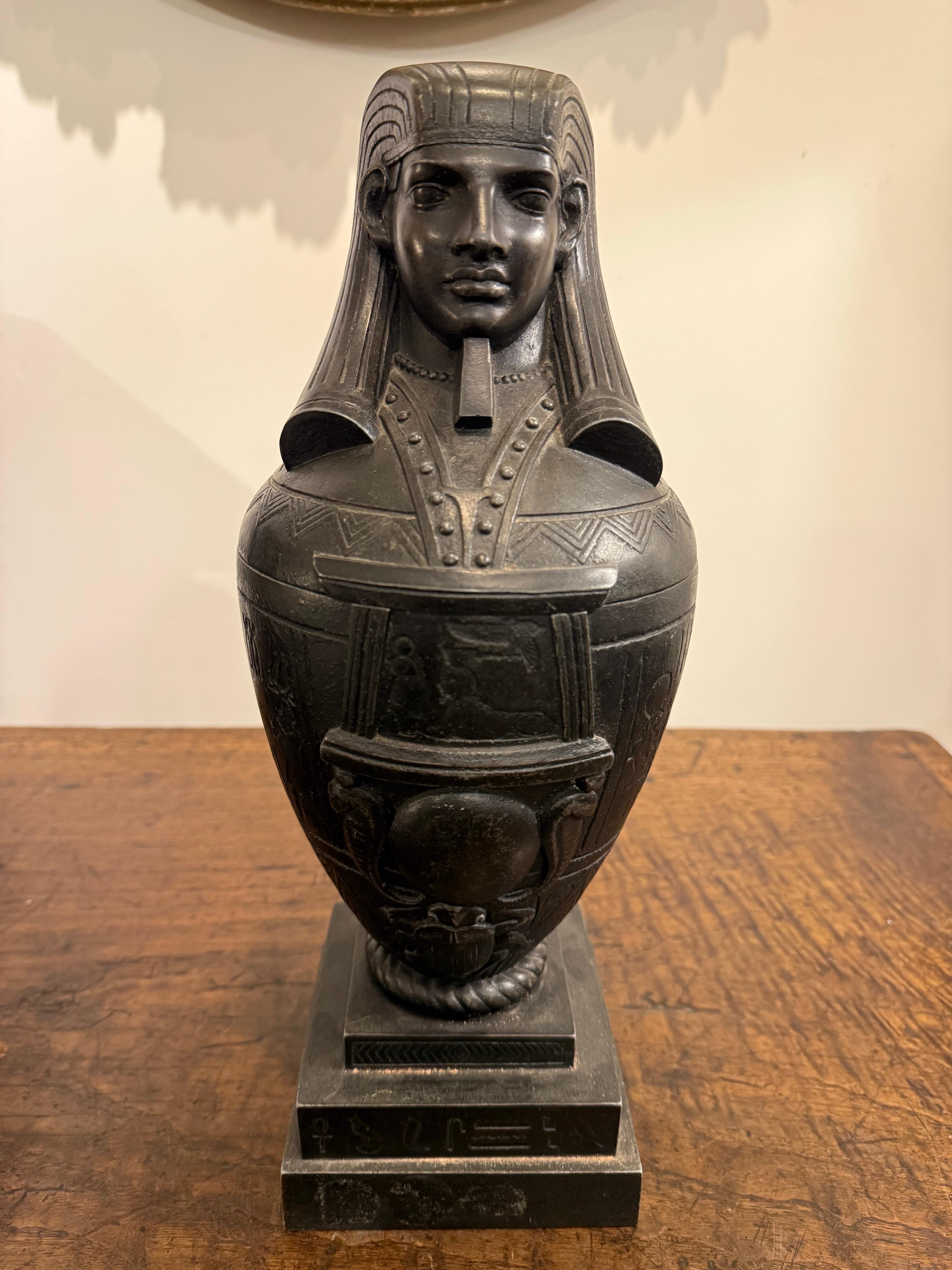 A Bronzed Metal Canopic Jar with Base, Early 20th Century

Description:
The jar with a lid in the form of a humanoid head wearing the pharaonic nemes headdress and false beard, identifying the figure as the god Imsety. One of the four sons of Horus,