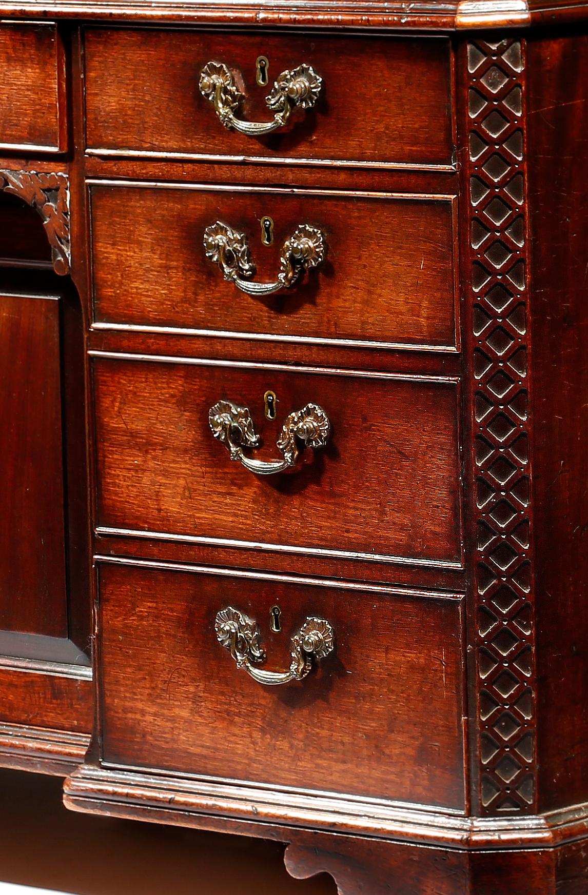 A George III Chippendale period mahogany knee-hole desk the well figured rectangular top with a thumb moulded edge, above banks of drawers, flanked by blind fret canted corners, resting on angled bracket feet, retaining its original brass handles,