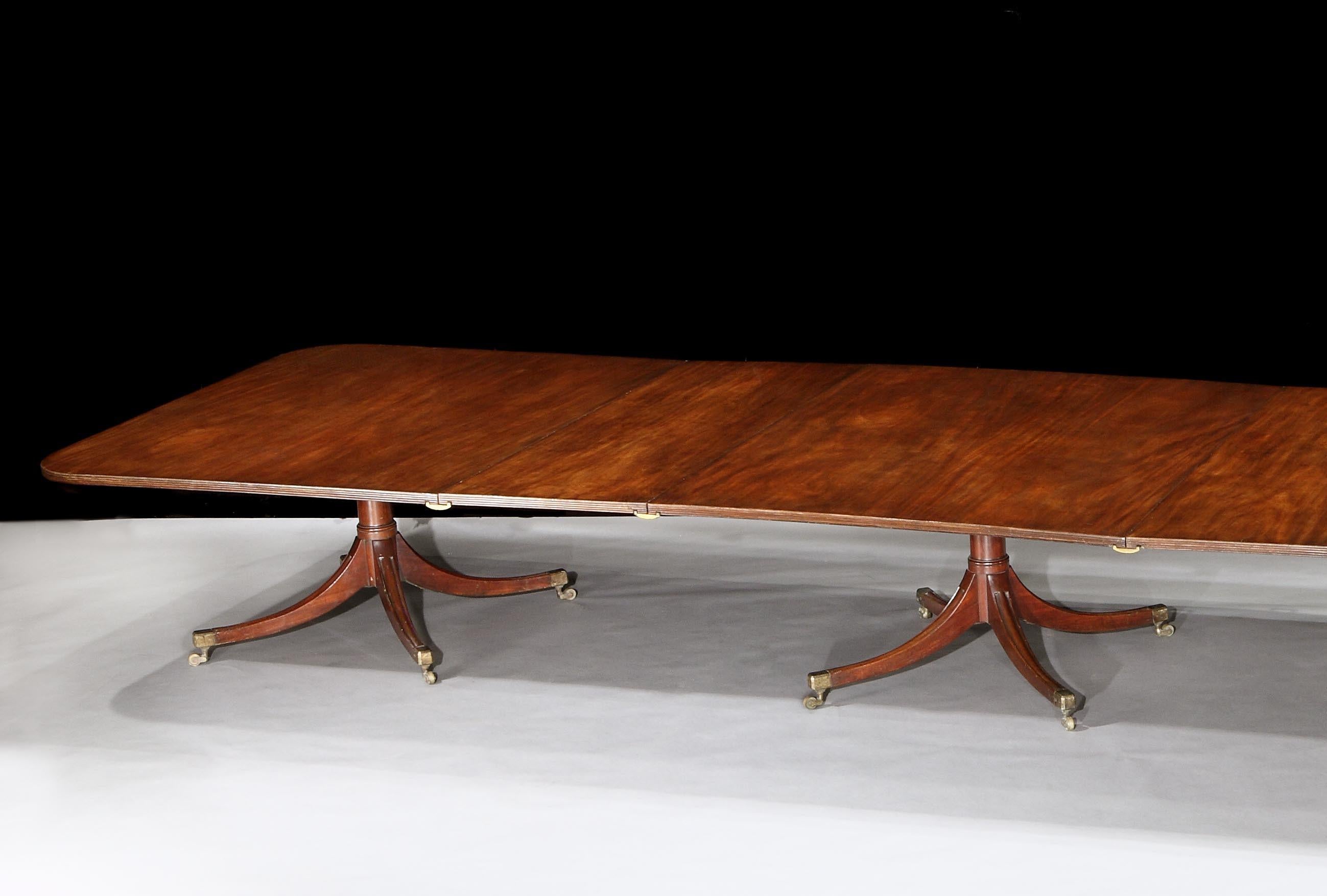 A fabulous George III mahogany four pedestal dining table, the superbly figured mahogany rectangular tops, with a reeded edge and three extra leaves, resting on four shot of turned gun barrel pedestals with brass box casters.