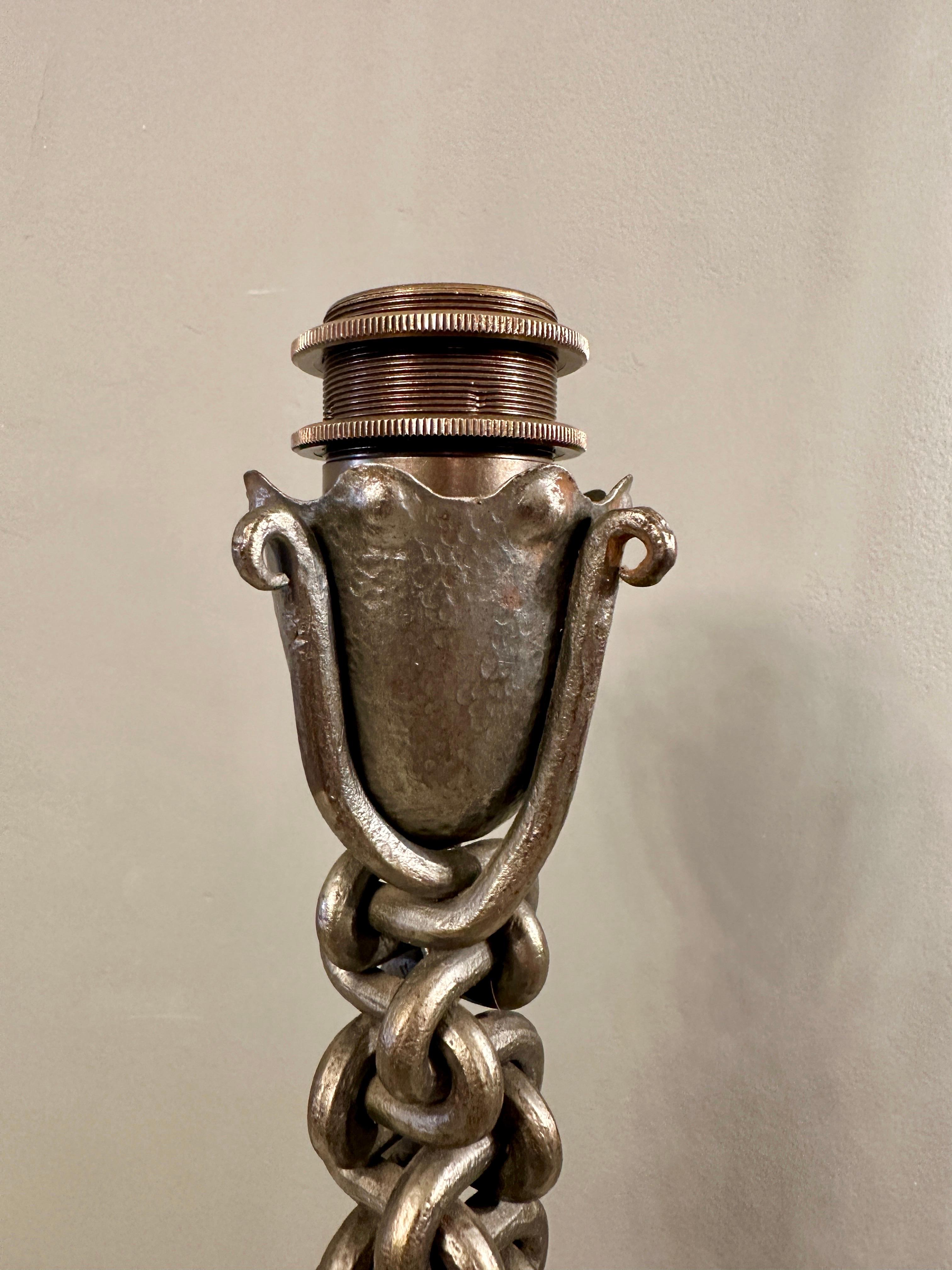 A tall wrought iron chain link table lamp in the brutalist manner. The decorative bulb holder with bronze unit inside and elephant grey re wired silk cord. Polished wrought iron finish with inter woven tapering chain link stem stood on four  shaped