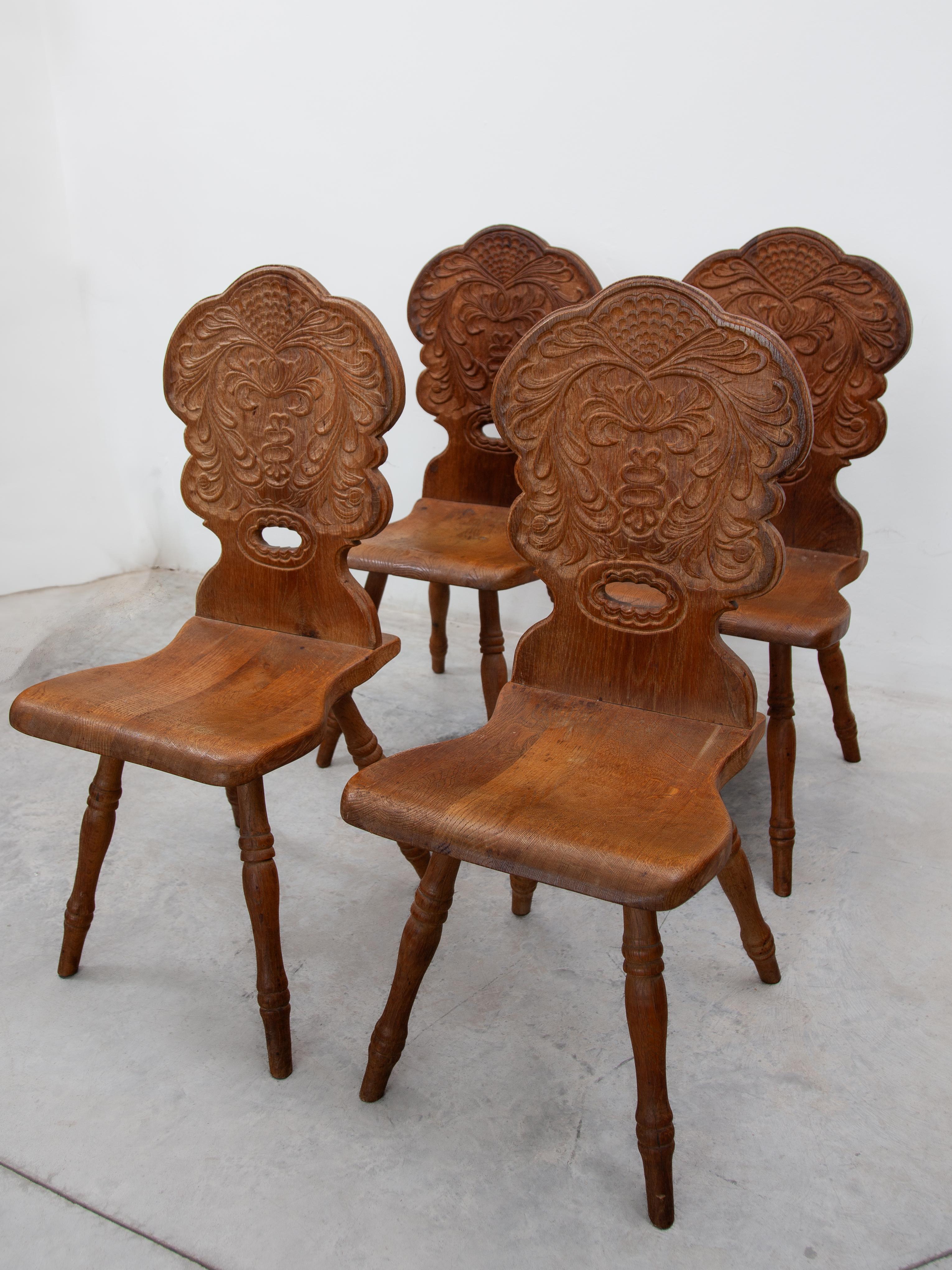 This beautiful set of four solid oak chairs features hand-carved, folk-style ornamentation of decorative leaf varieties in a rustic alpine atmosphere. The tapered seat is supported by round, hand-carved legs, giving the chair a solid yet elegant
