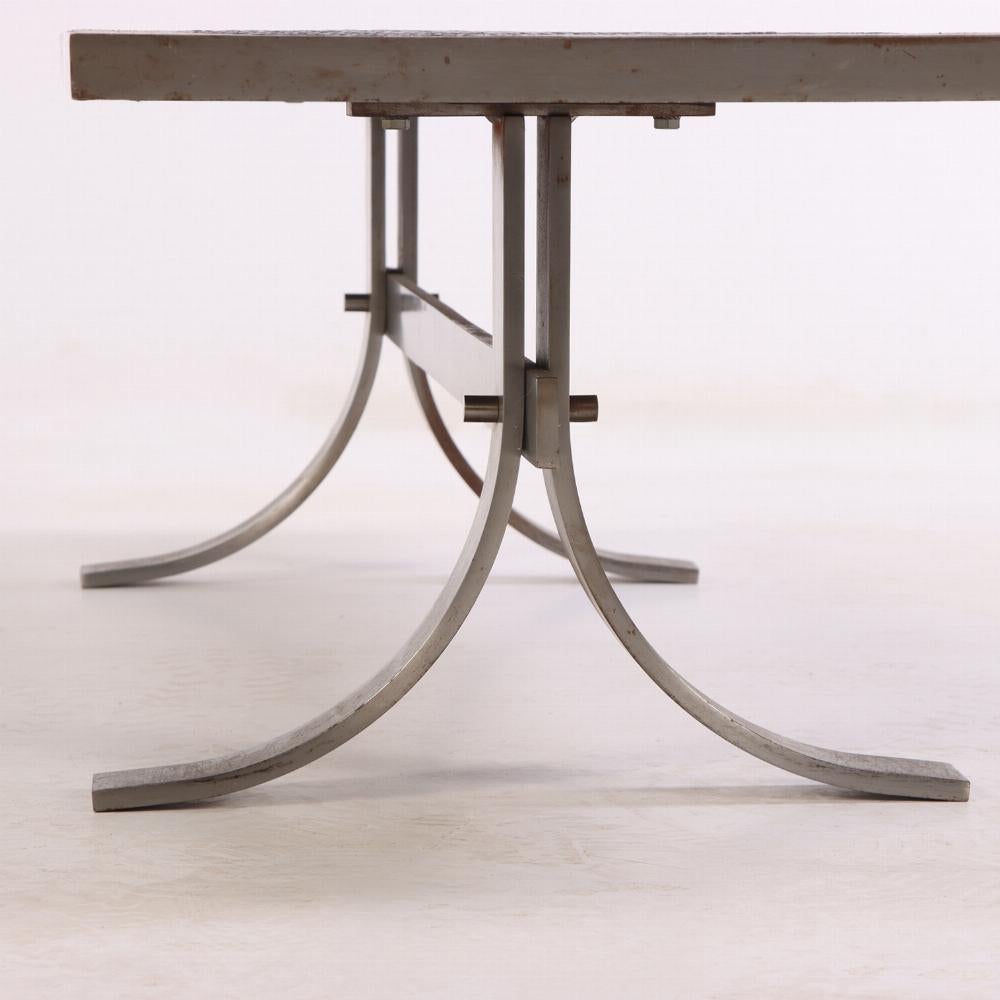 The table features a steel frame with an inset ceramic tile top, showcasing D’Haenens’ signature fusion of raw materiality and refined artistry. With its bold textured circular design and sculptural presence, this rectangular table supported by 