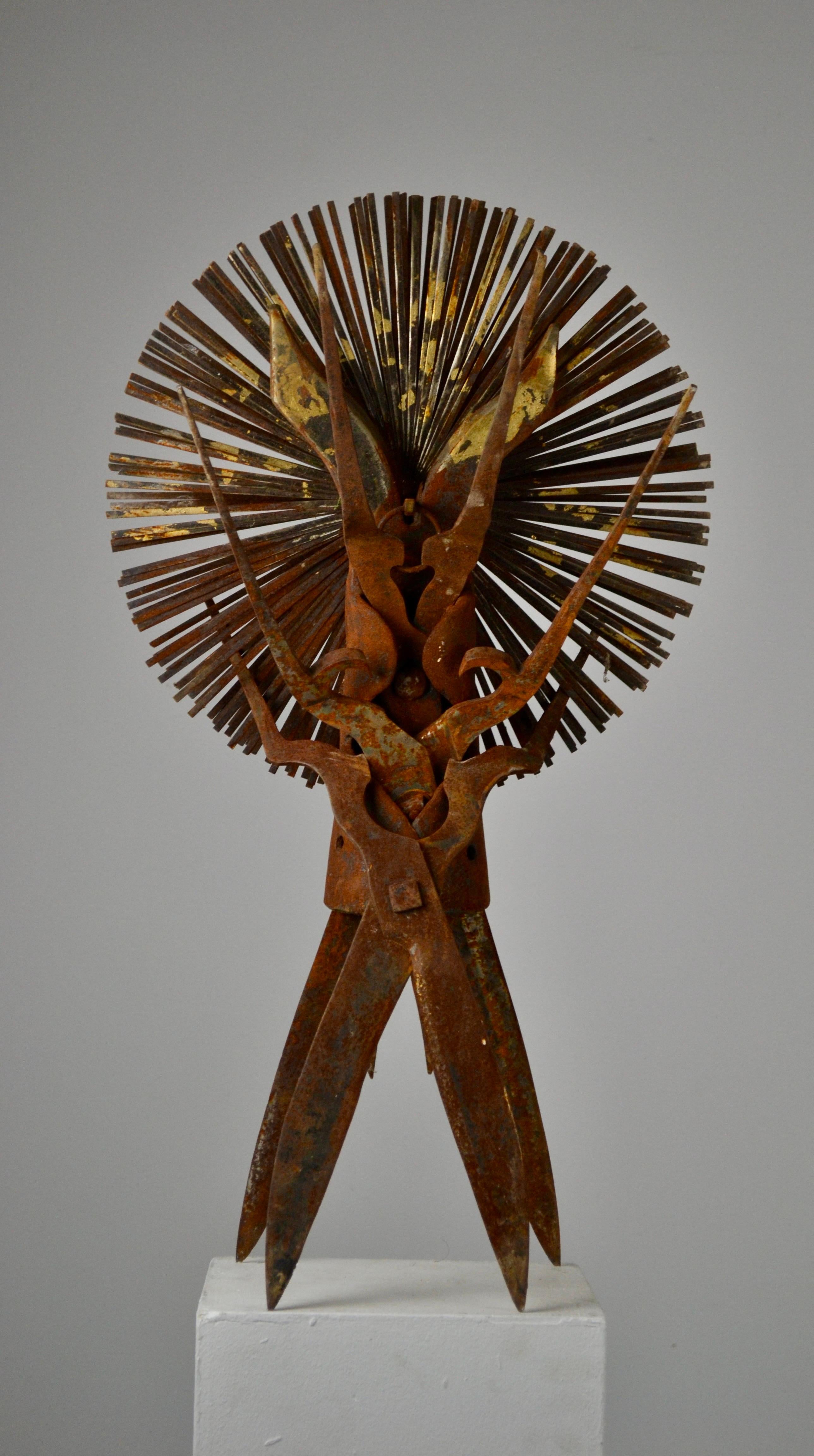This metal sculpture by Gilbert Ségas depicts an anthropomorphic figure with a totemic presence, assembled from old tools. Two large crossed shears form the legs, while pliers and other metallic elements shape the torso and raised arms, suggesting a