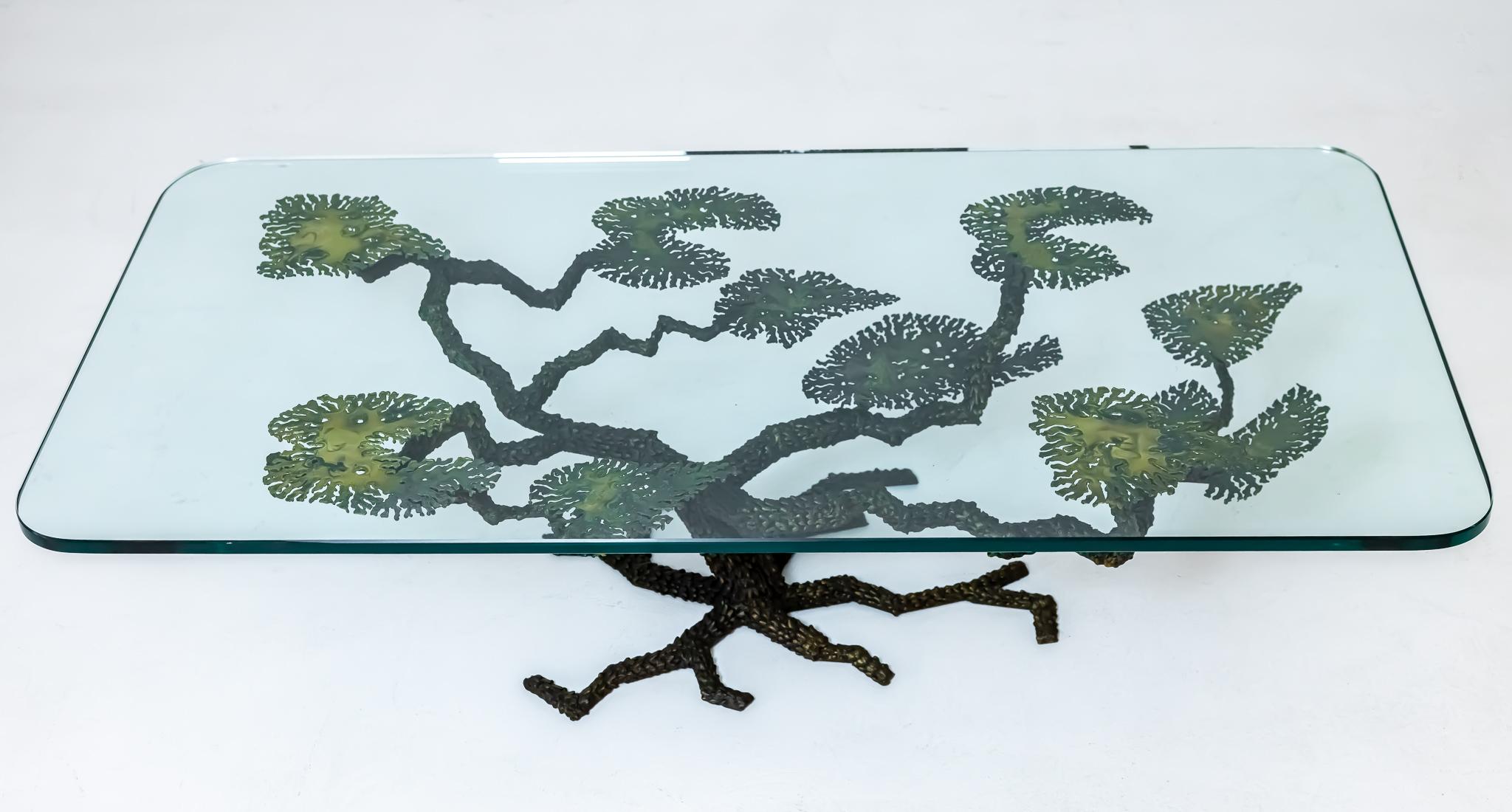 This glass topped cocktail table features a metal base that includes torch cut leaves and a trunk and roots that have been enhanced using solder. Table is very much in the style of Silas Seandel but is not signed. This table has a beautiful patina,