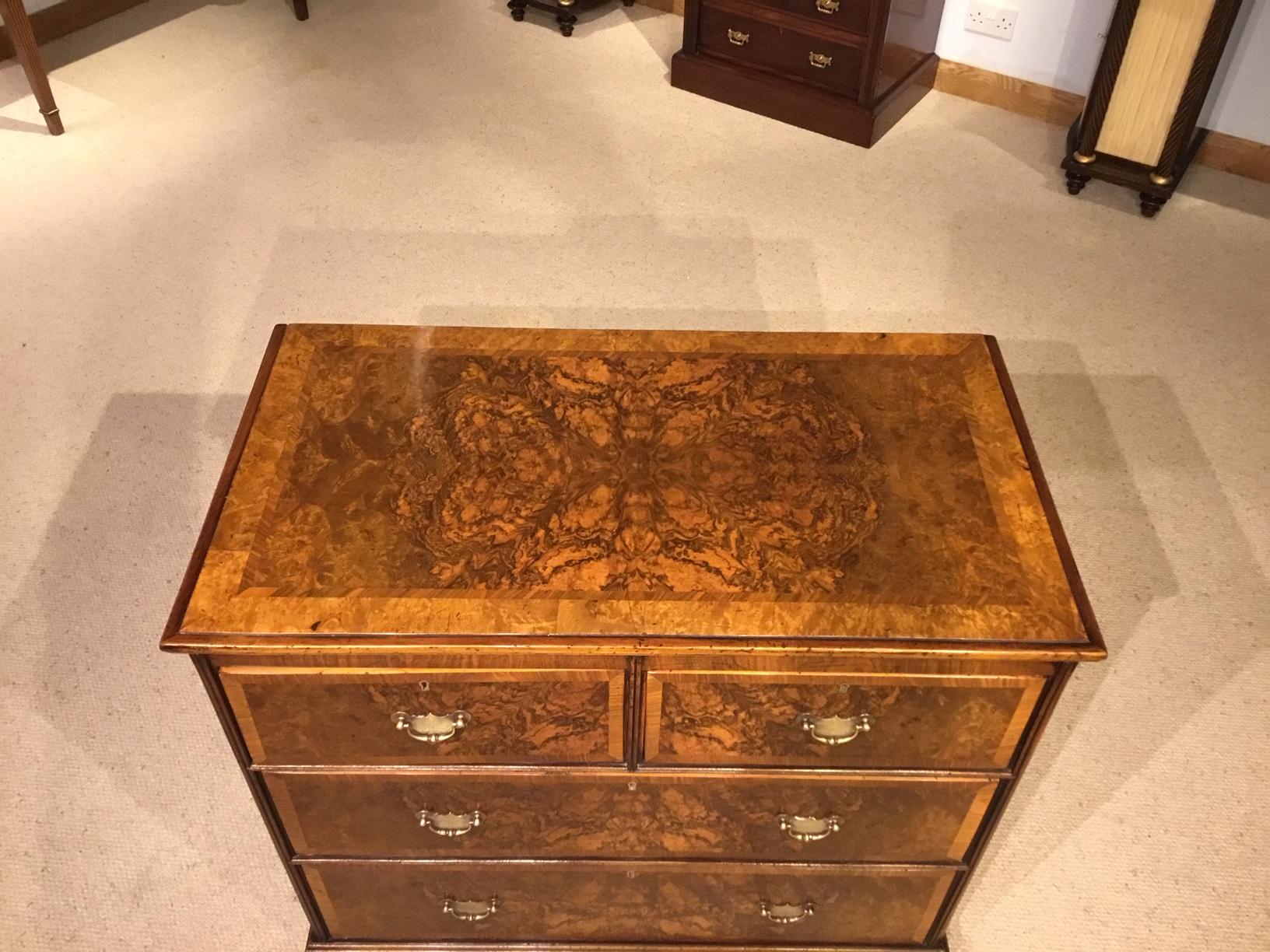 A burr walnut Georgian style antique chest of drawers by Heals of London. Having a rectangular top veneered in burr walnut with walnut banding above an arrangement of two short and two long rectangular drawers with beautifully veneered burr walnut