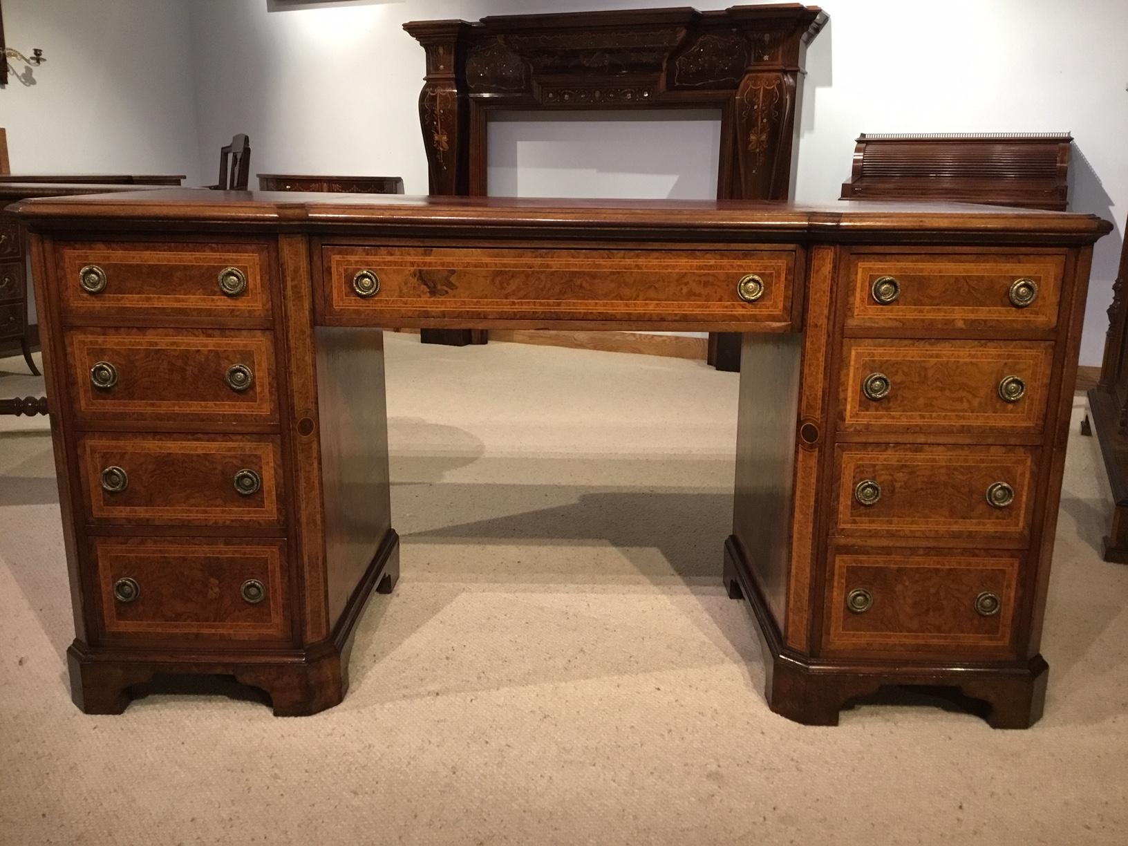 A burr walnut, kingwood and amboyna Victorian period antique writing desk. The rectangular top with a red inset writing surface, banded in burr walnut and with a slightly inverted breakfront. Having an arrangement of nine mahogany lined drawers with