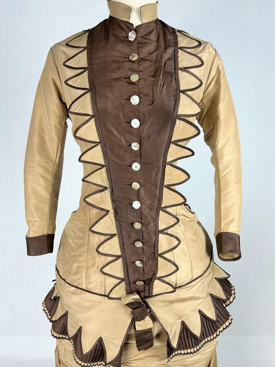 Circa 1880-1885 
Stati Uniti

Abito a gabbia con risvolto, linea a principessa in due parti, corpetto a balena e gonna risvoltabile in taffetà di seta beige e marrone. Corpetto curvo, girocollo e maniche lunghe angolate, chiuse sul davanti con