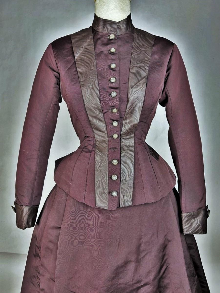 Circa 1880-1890
France
Day dress with integrated Bustle cage, by petite Bourgoisie, bodice and skirt in aubergine/chocolate silk faille, trimmed with chestnut moiré and dating from the golden age of the Impressionists. Curved bodice with darts,