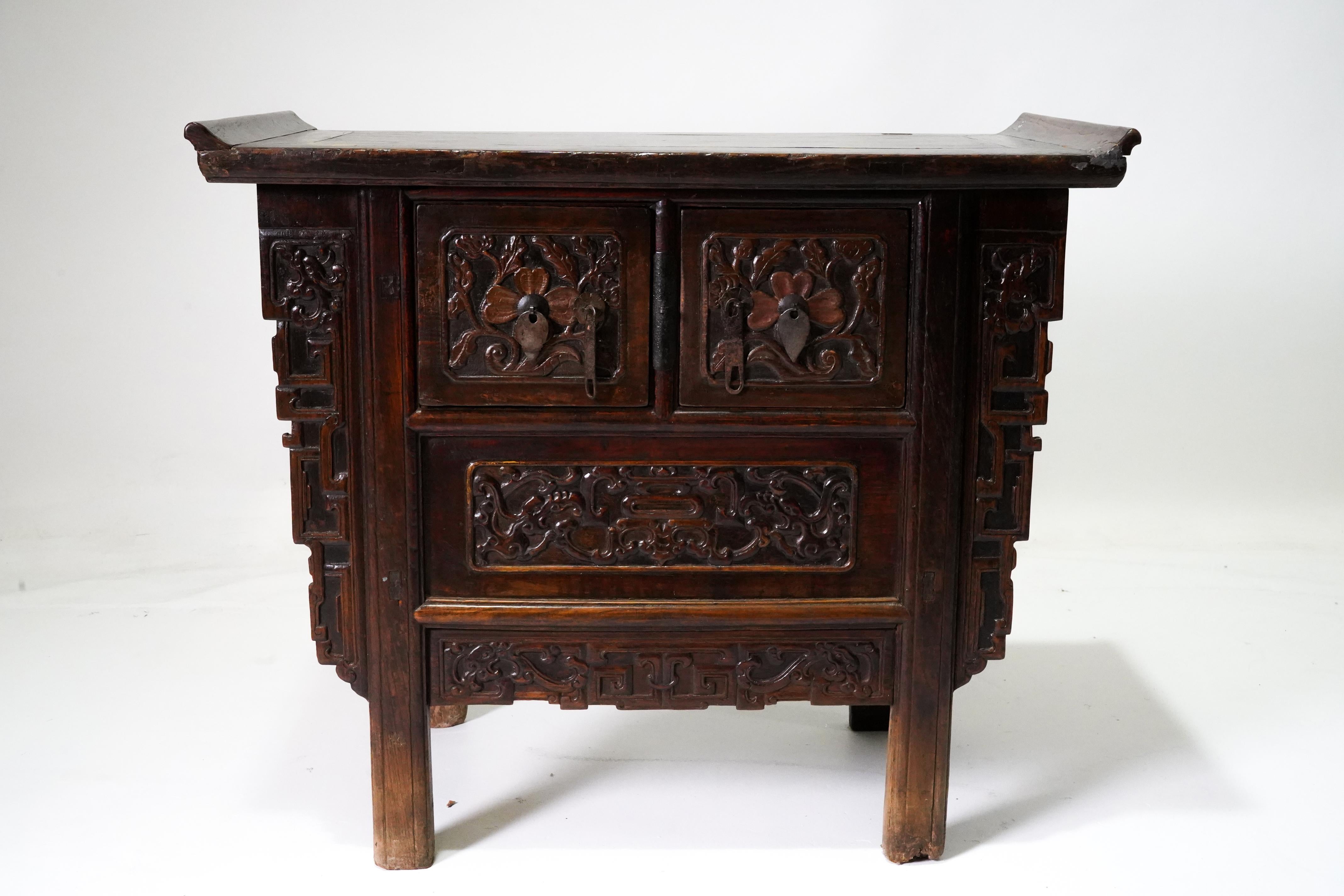 A Chinese Qing wooden butterfly cabinet from the 19th century, with carved spandrels, drawers, doors and a dark oxblood patina. This elegant small coffer, sometimes called a butterfly cabinet, features a floating panel top sitting above two carved