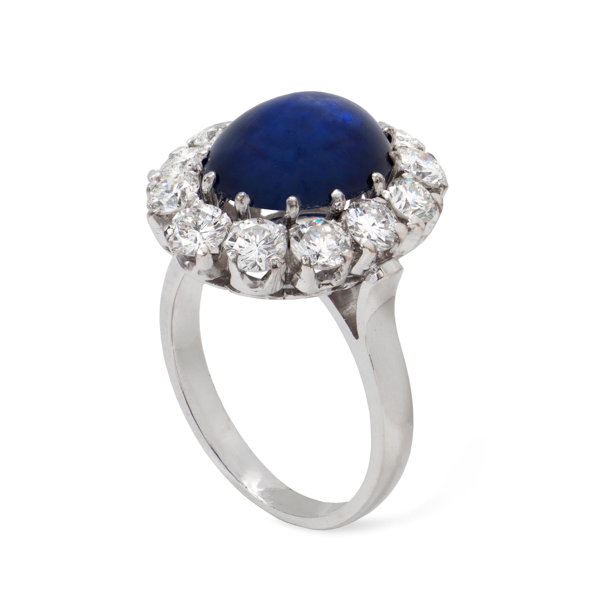 A cabochon sapphire and diamond cluster ring, the oval cabochon sapphire weighing 5.11 carats, surrounded by twelve round brilliant-cut diamonds estimated to weigh 2 carats in total, all claw-set in white gold mount, later-hallmarked 18ct London,